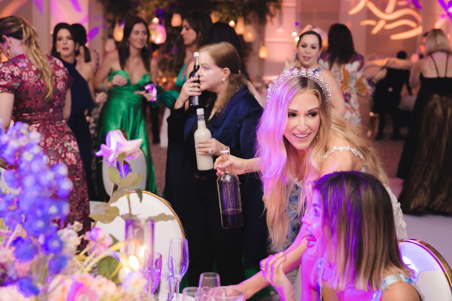Party guests enjoying a vibrant celebration with purple lighting and floral decorations at an elegant evening event.