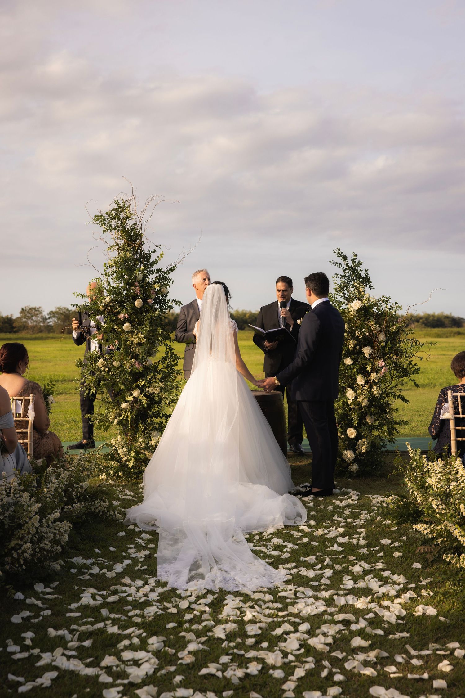 An outdoor wedding ceremony setup with flower petals scattered on the ground and greenery decorations.
