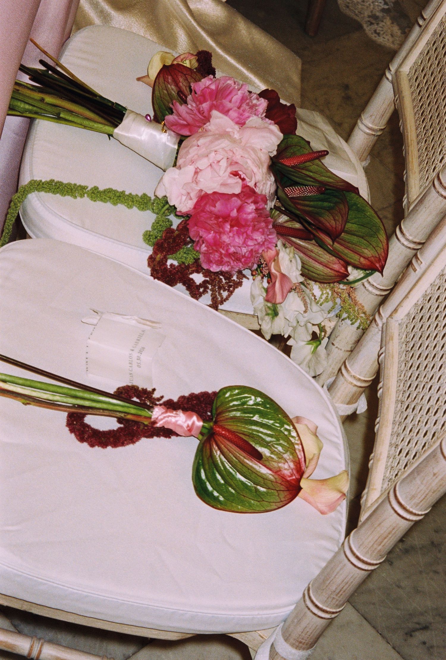 Elegant wedding bouquets with pink peonies and tropical anthurium flowers arranged on white chairs.