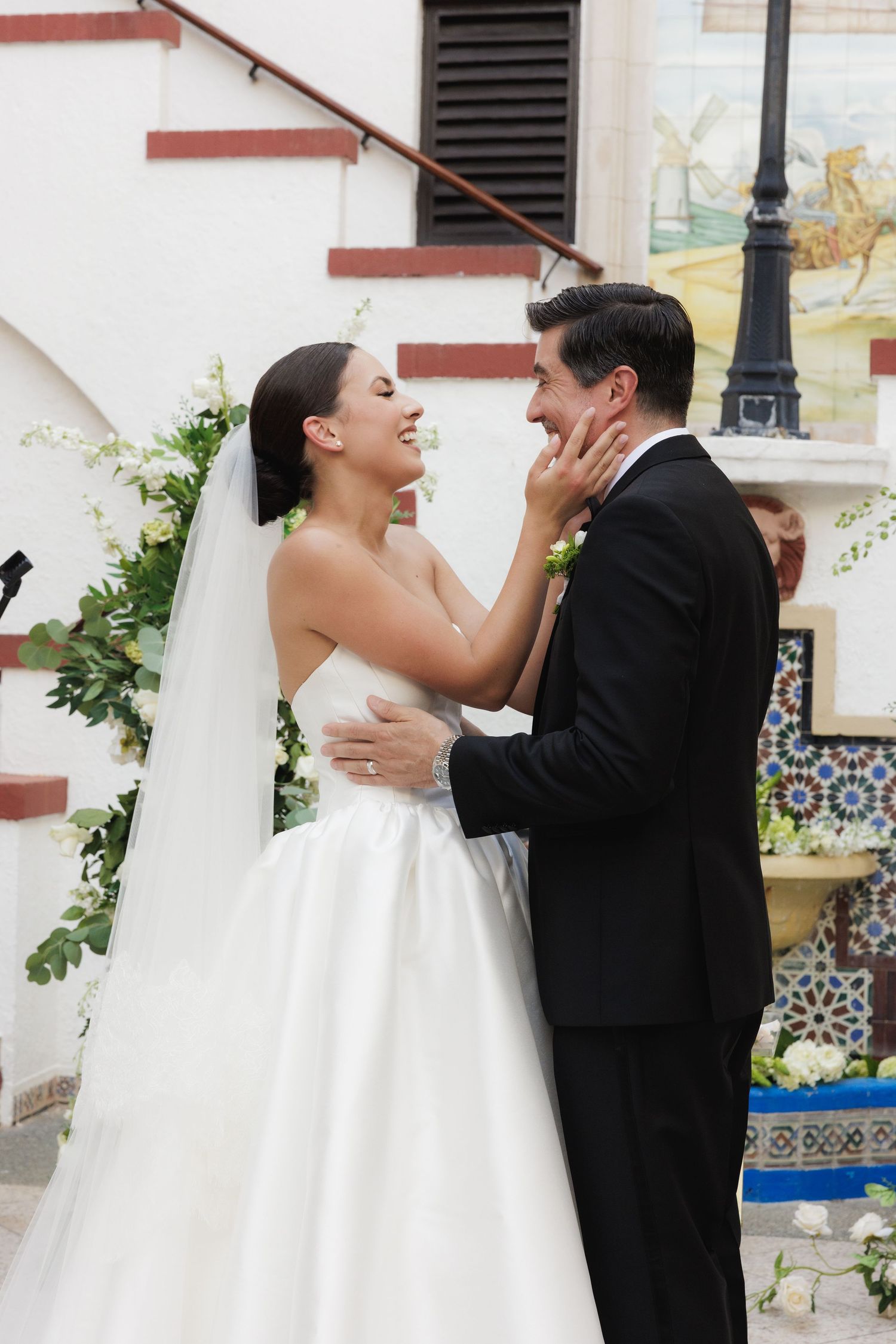 Joyful wedding moment captured as couple embraces on decorated steps with Spanish tile details.