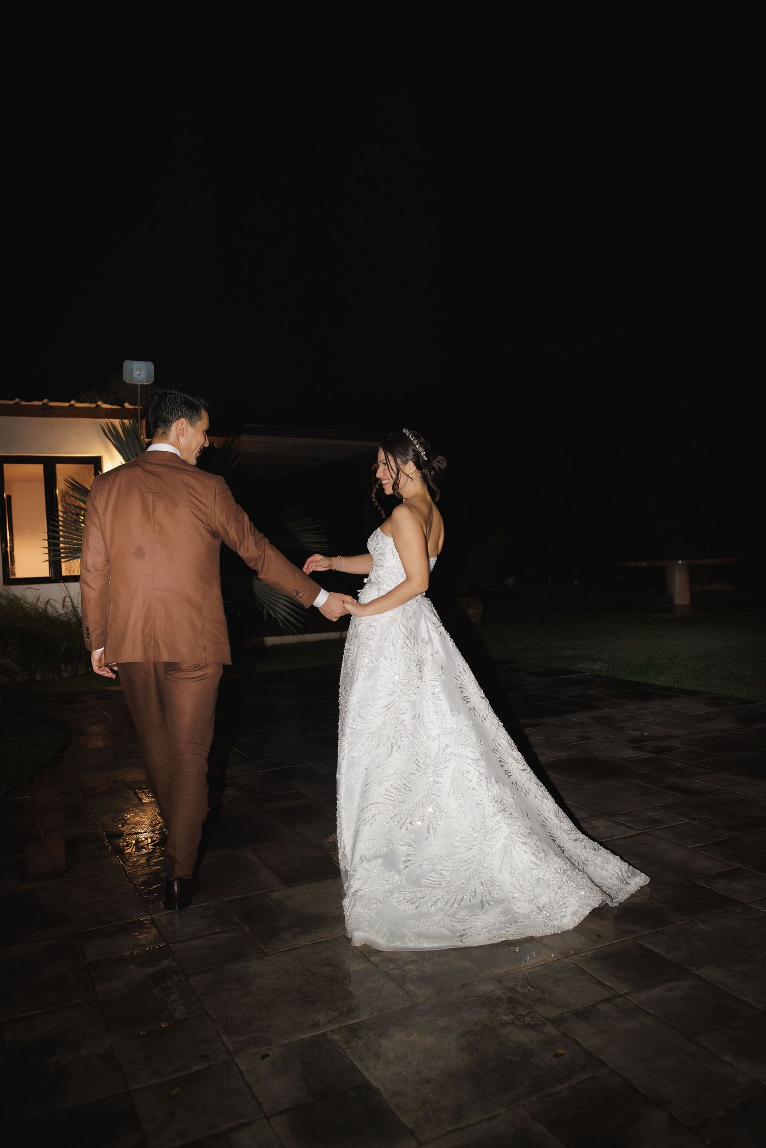Bride and groom dance together on a dark outdoor patio during their wedding reception.