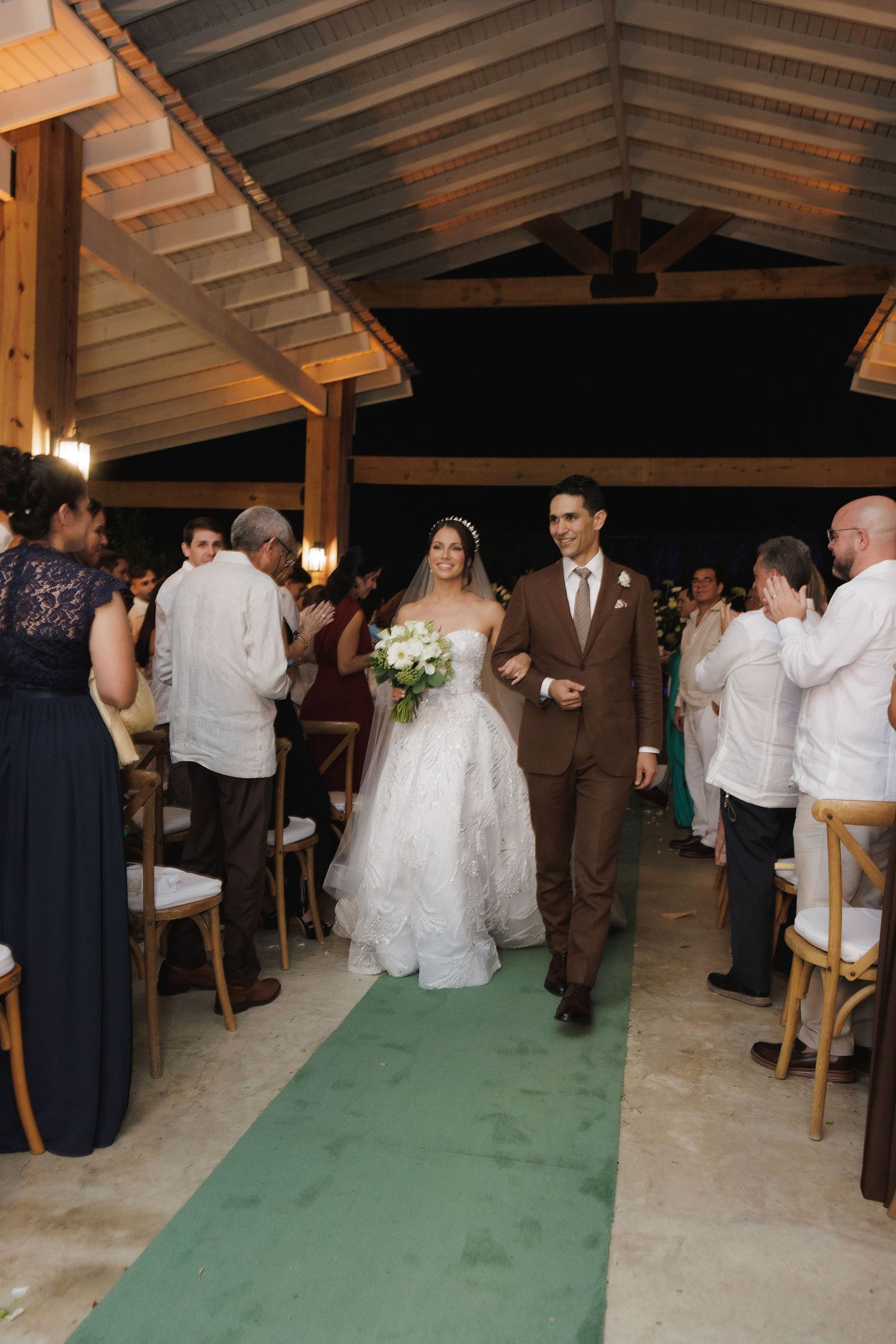Reception celebration in a wooden pavilion with guests dancing on a green carpet.