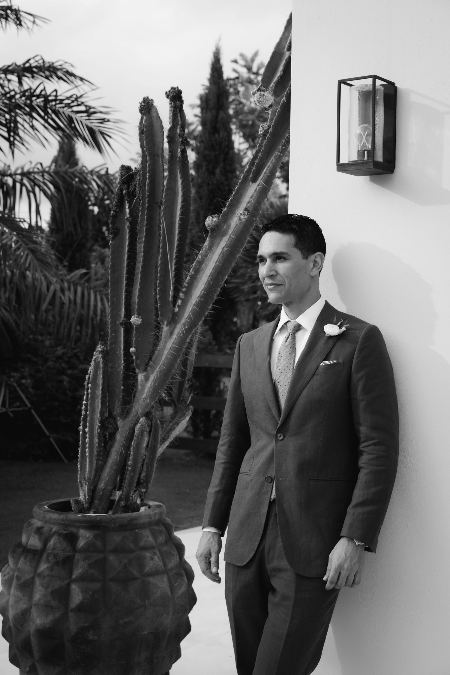 A series of black and white portraits showing people in formal attire against a white wall with palm trees visible.
