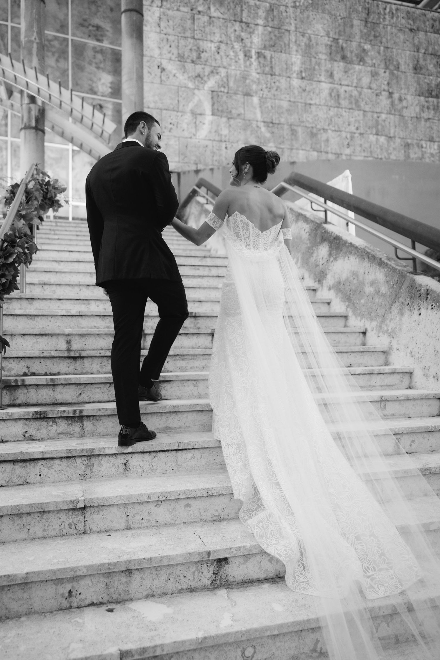 Wedding dress train flows elegantly down stone steps in black and white photograph.