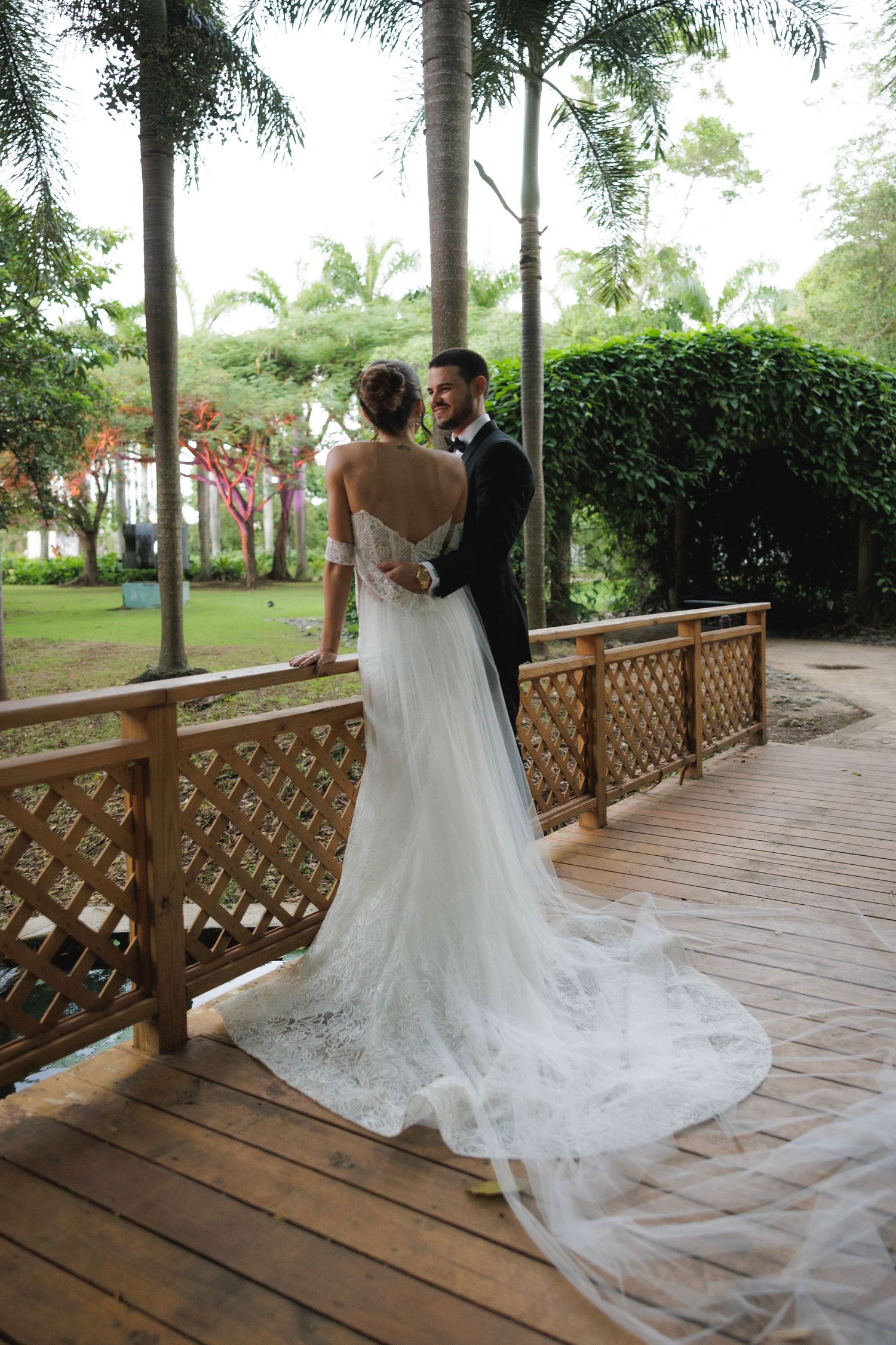 A romantic wedding couple dances on a wooden deck surrounded by tropical palm trees and lattice railings.