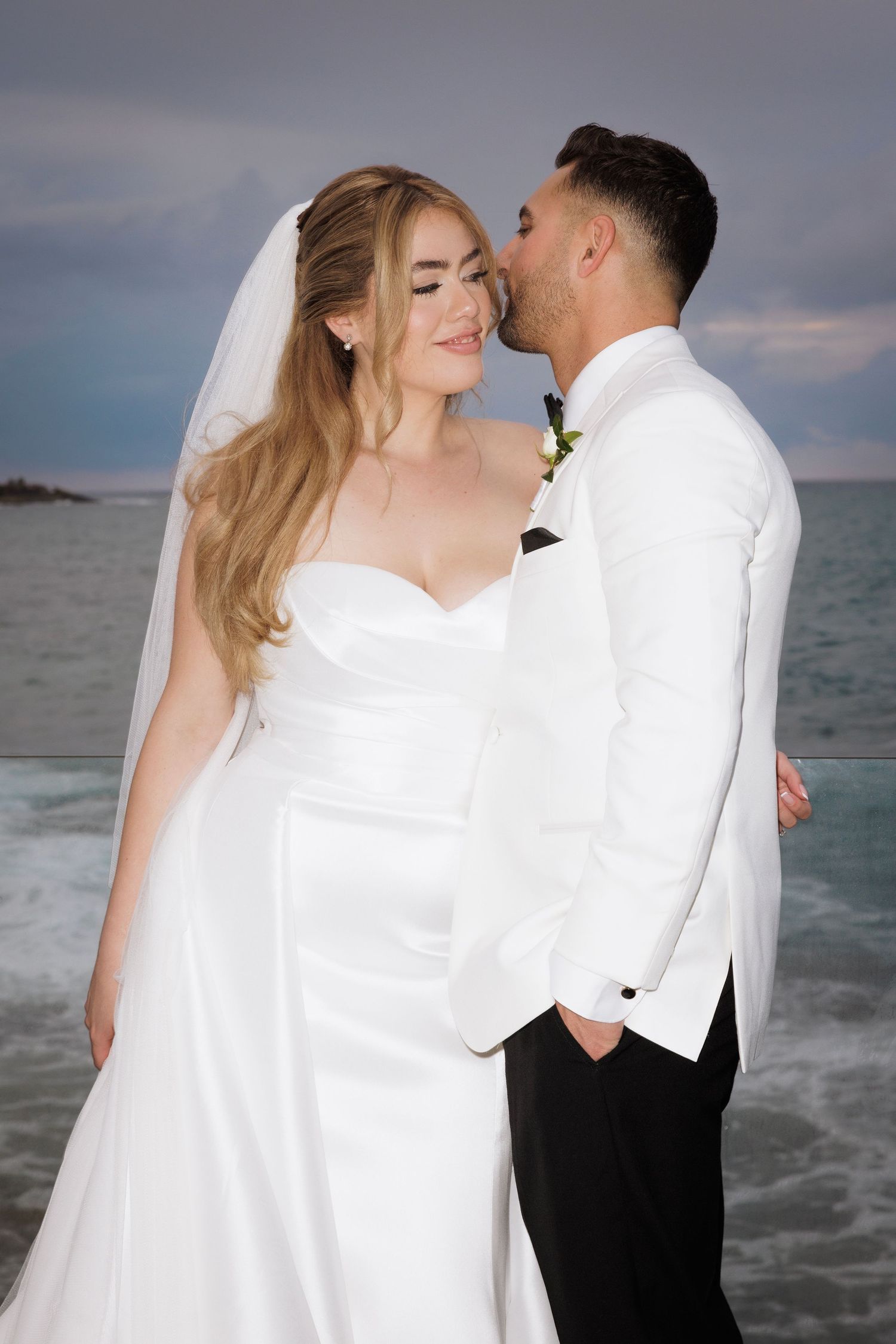 A romantic seaside wedding photoshoot featuring a couple in black and white attire against an ocean backdrop.