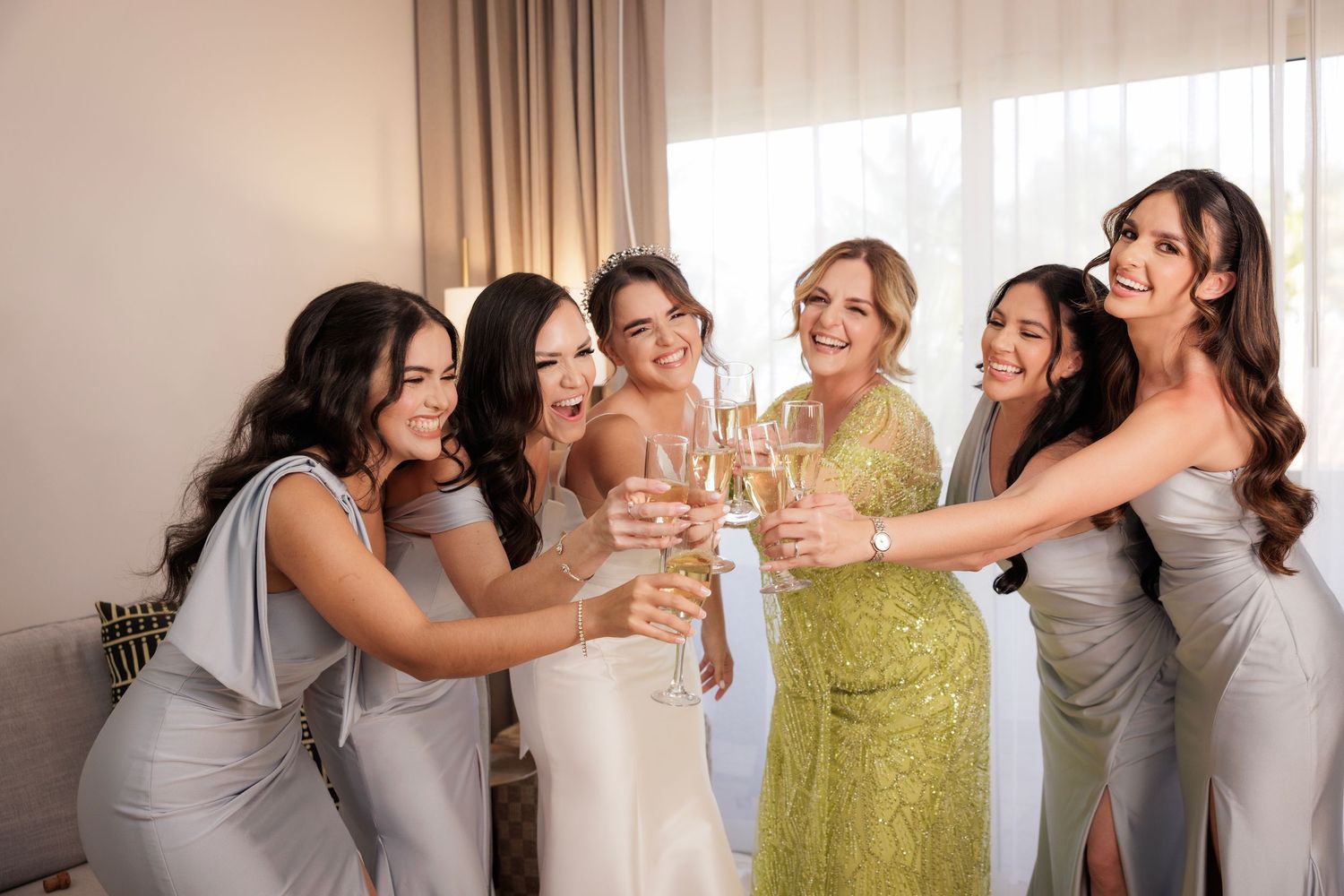 Bridesmaids in silver dresses gather around someone in a yellow dress for a celebratory toast.