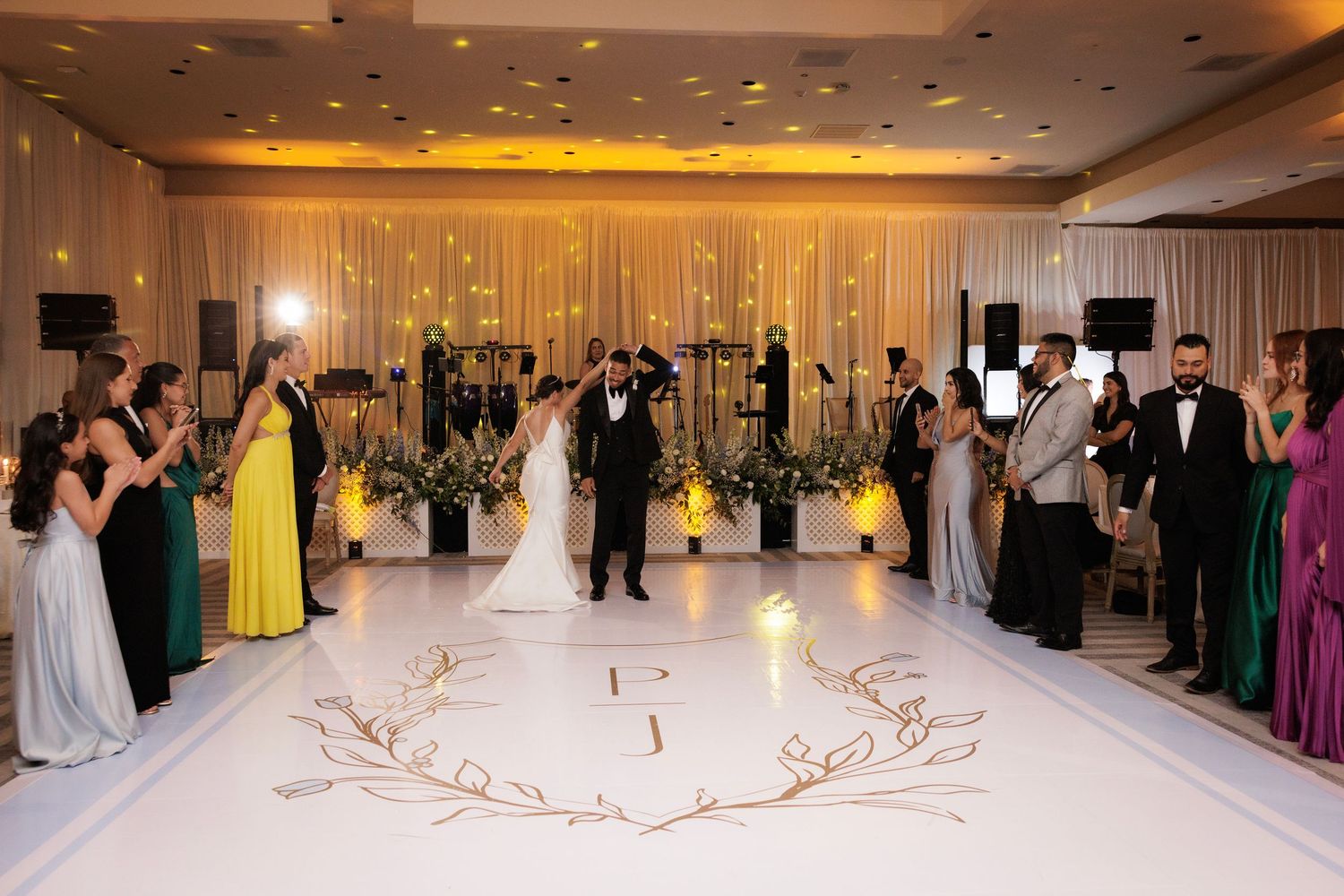 A panoramic view of an elegant wedding reception venue with yellow and white decor, glittering chandeliers, and dancing.