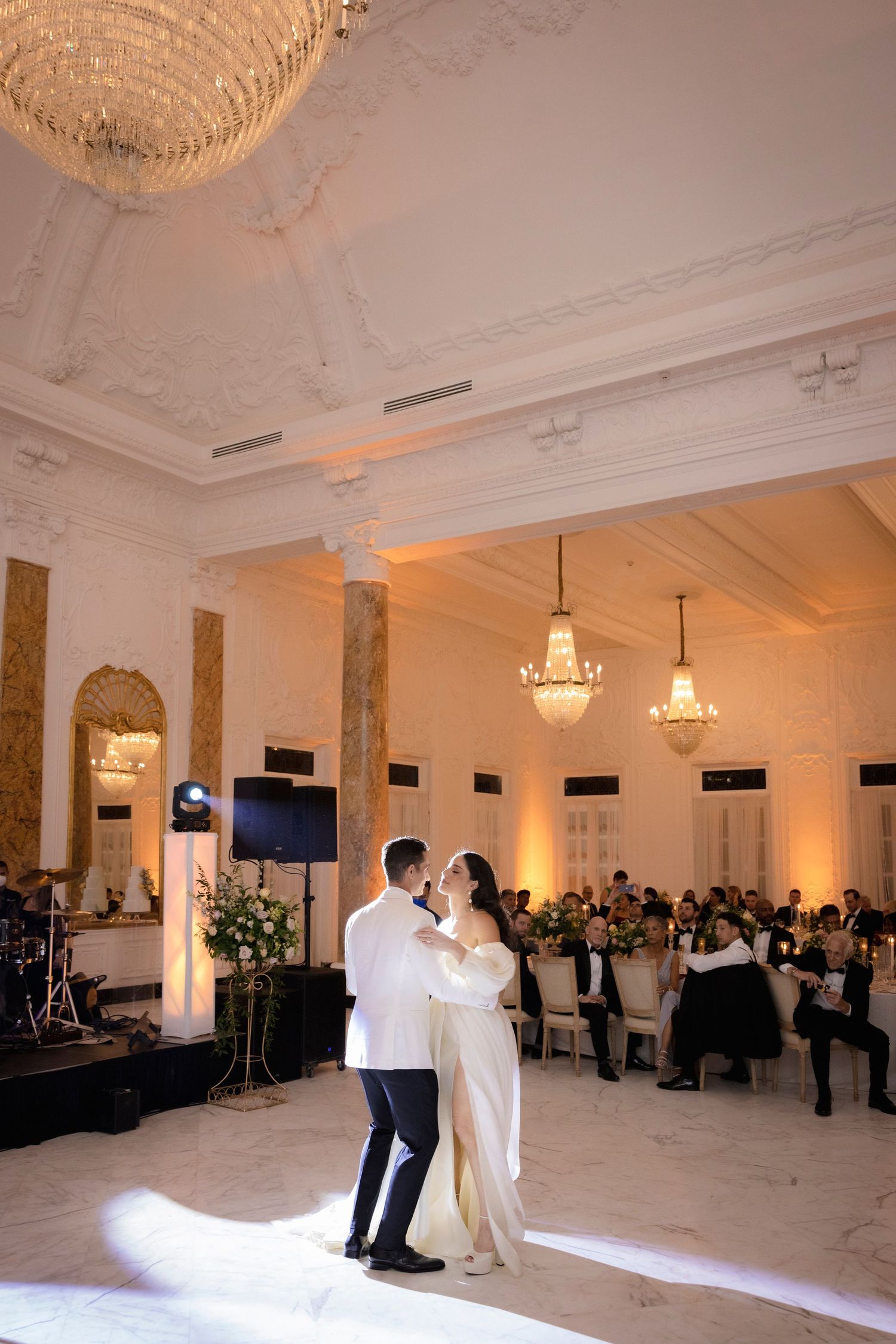 First dance in an elegant ballroom with crystal chandeliers and ornate ceiling details.