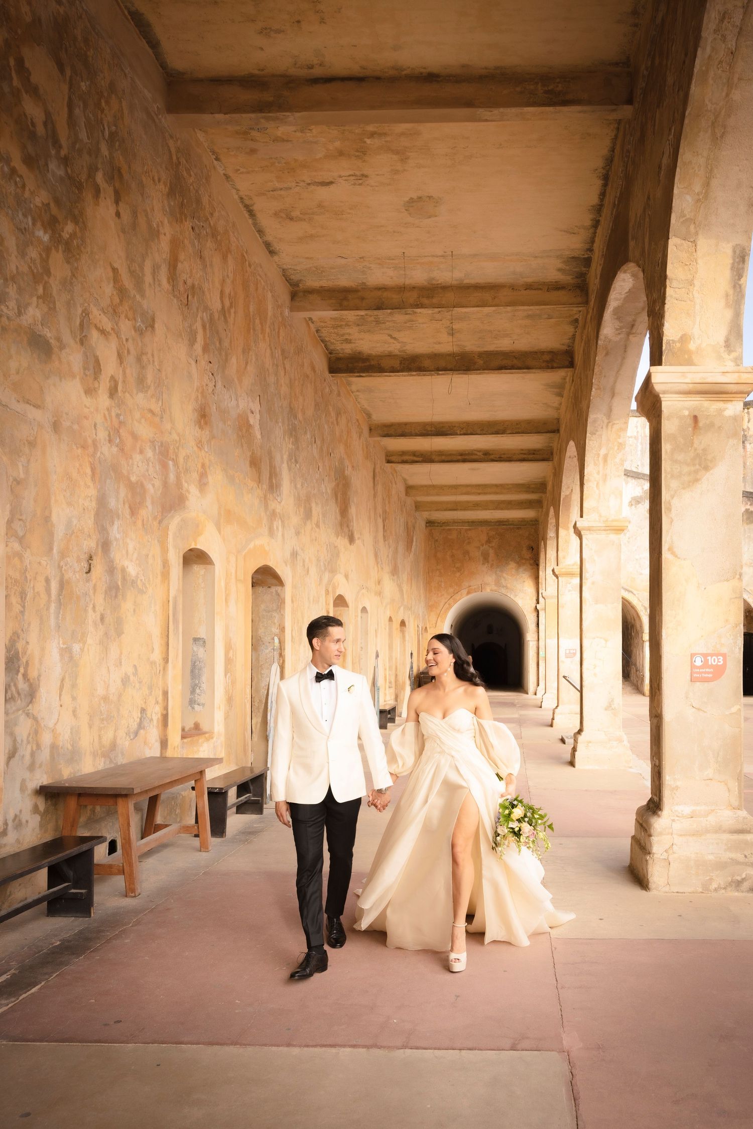 Elegant wedding photo session in a historic stone corridor with wooden beam ceiling.