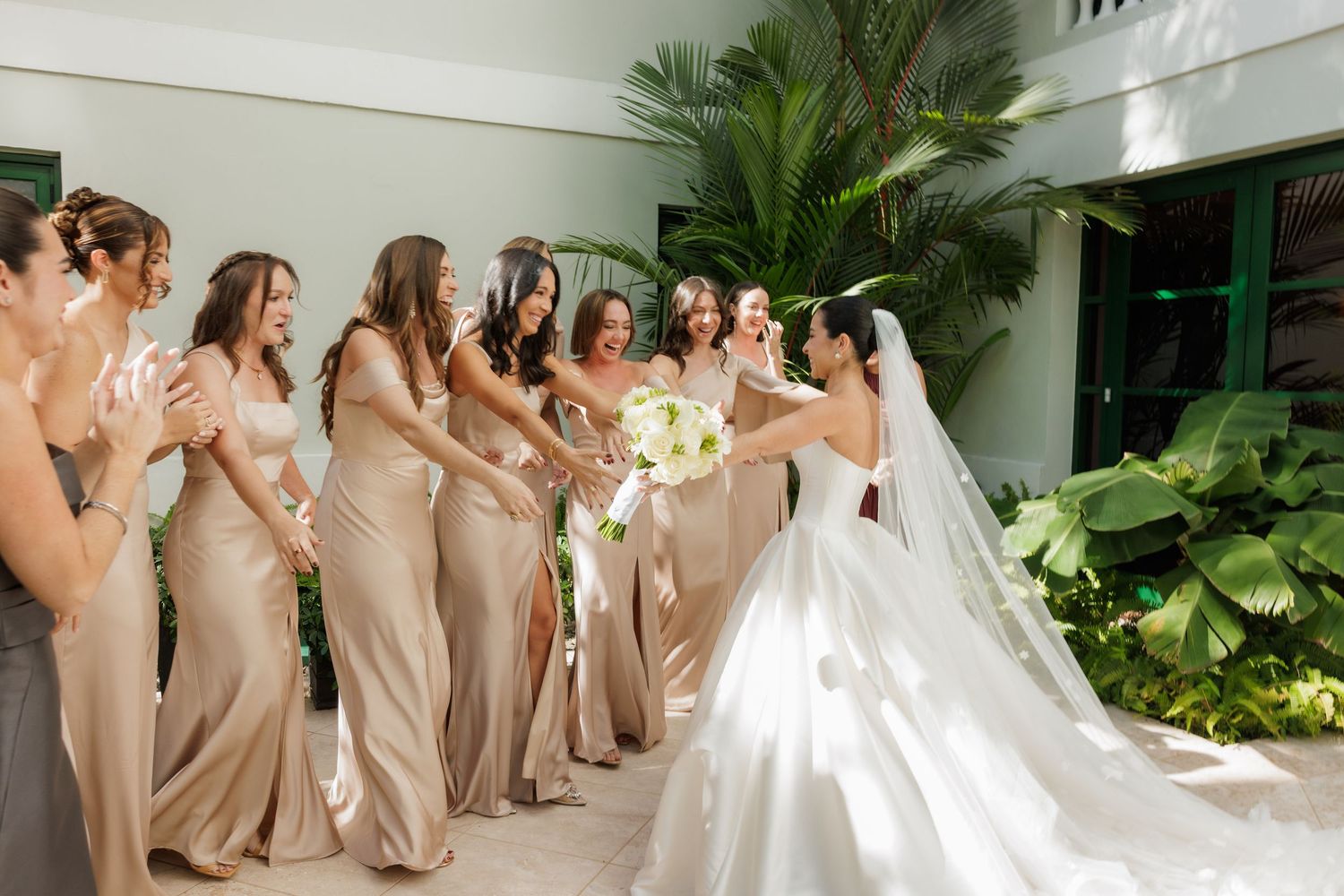 Bridesmaids in champagne dresses pose with bride in white gown during outdoor wedding celebration.