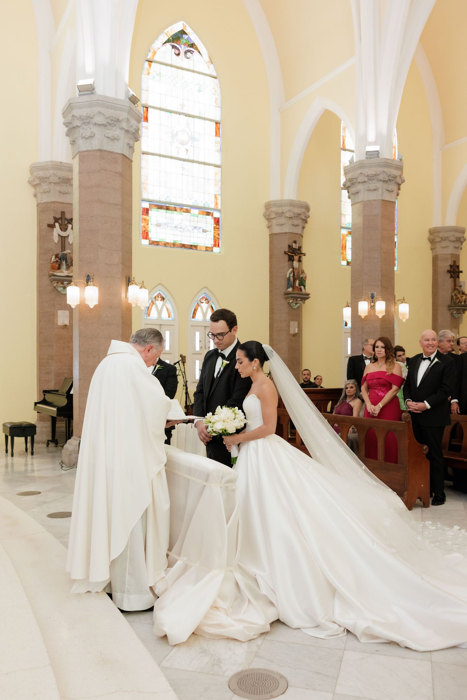 Traditional Catholic wedding ceremony takes place in a grand church with ornate stone columns and stained glass windows.
