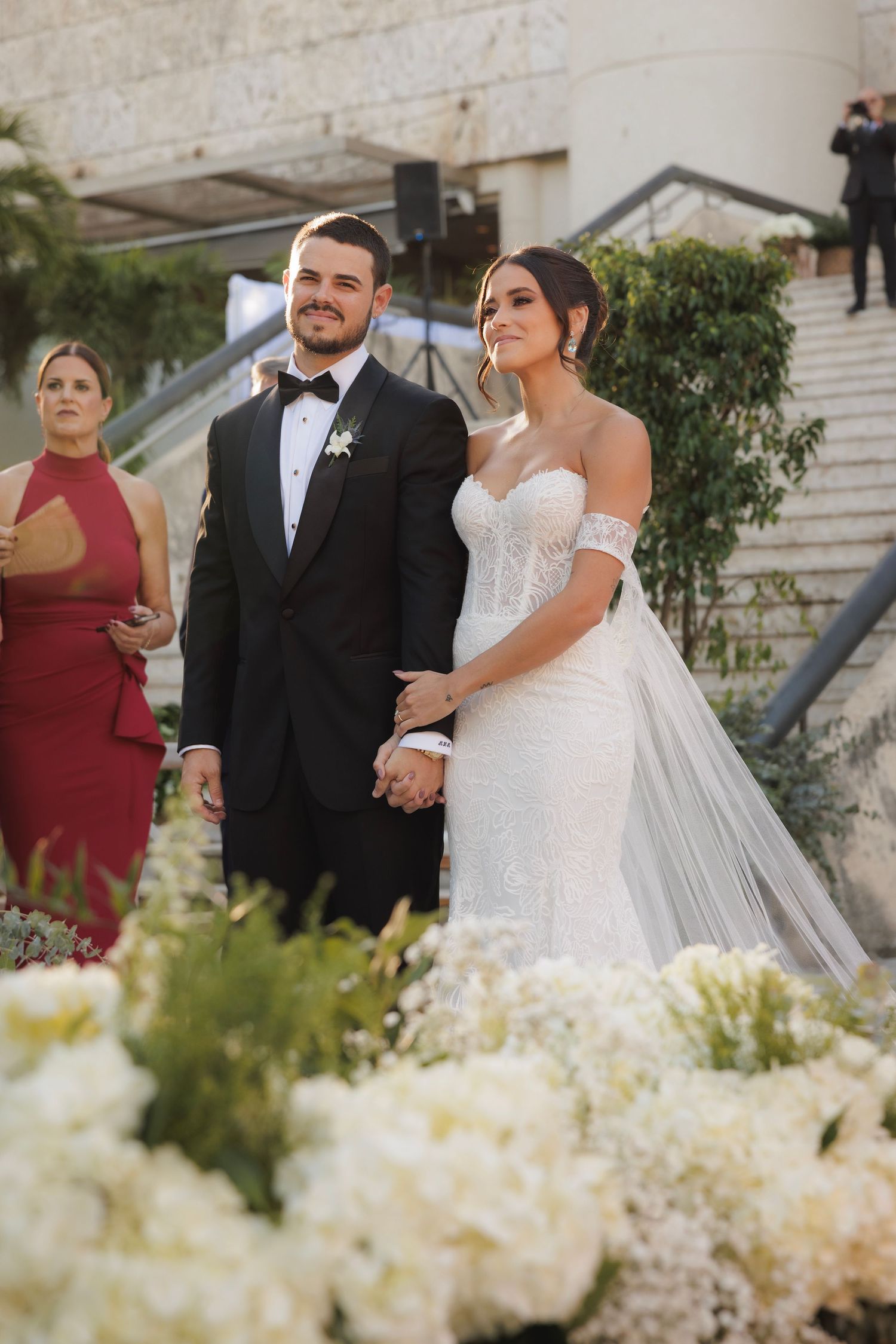 A romantic wedding ceremony with a couple in formal attire standing together surrounded by white floral arrangements.