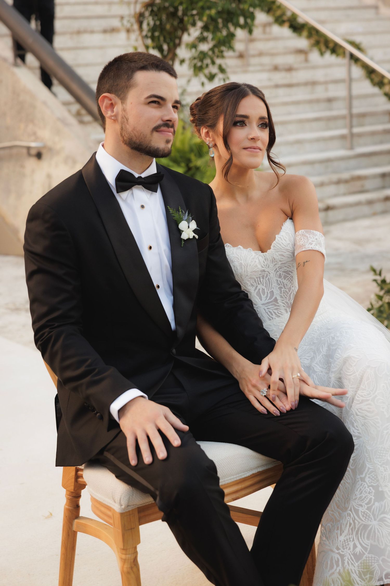 Candid wedding moment on wooden chairs during an outdoor celebration.