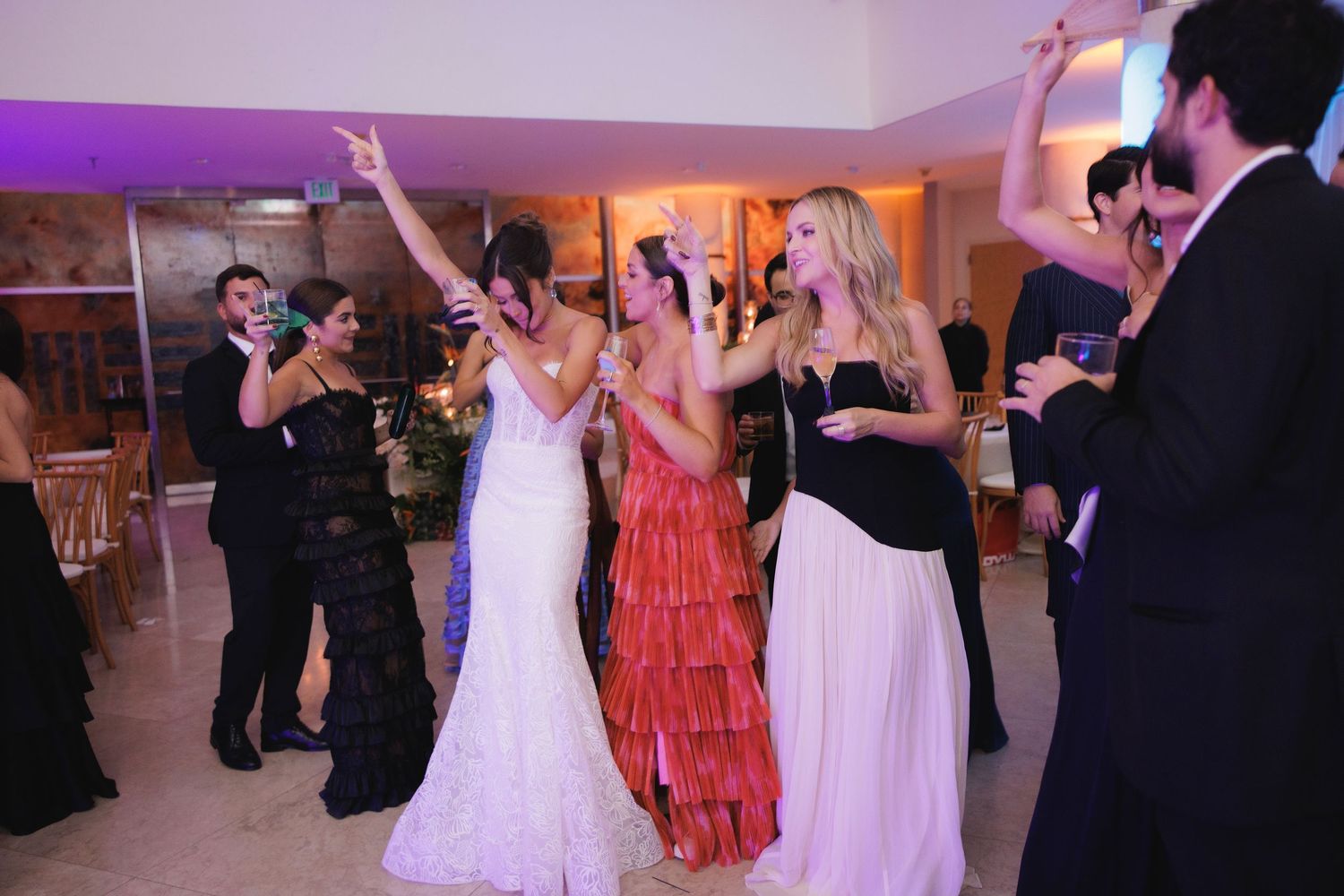 Wedding guests dancing and celebrating on the dance floor with colorful lighting and formal attire.