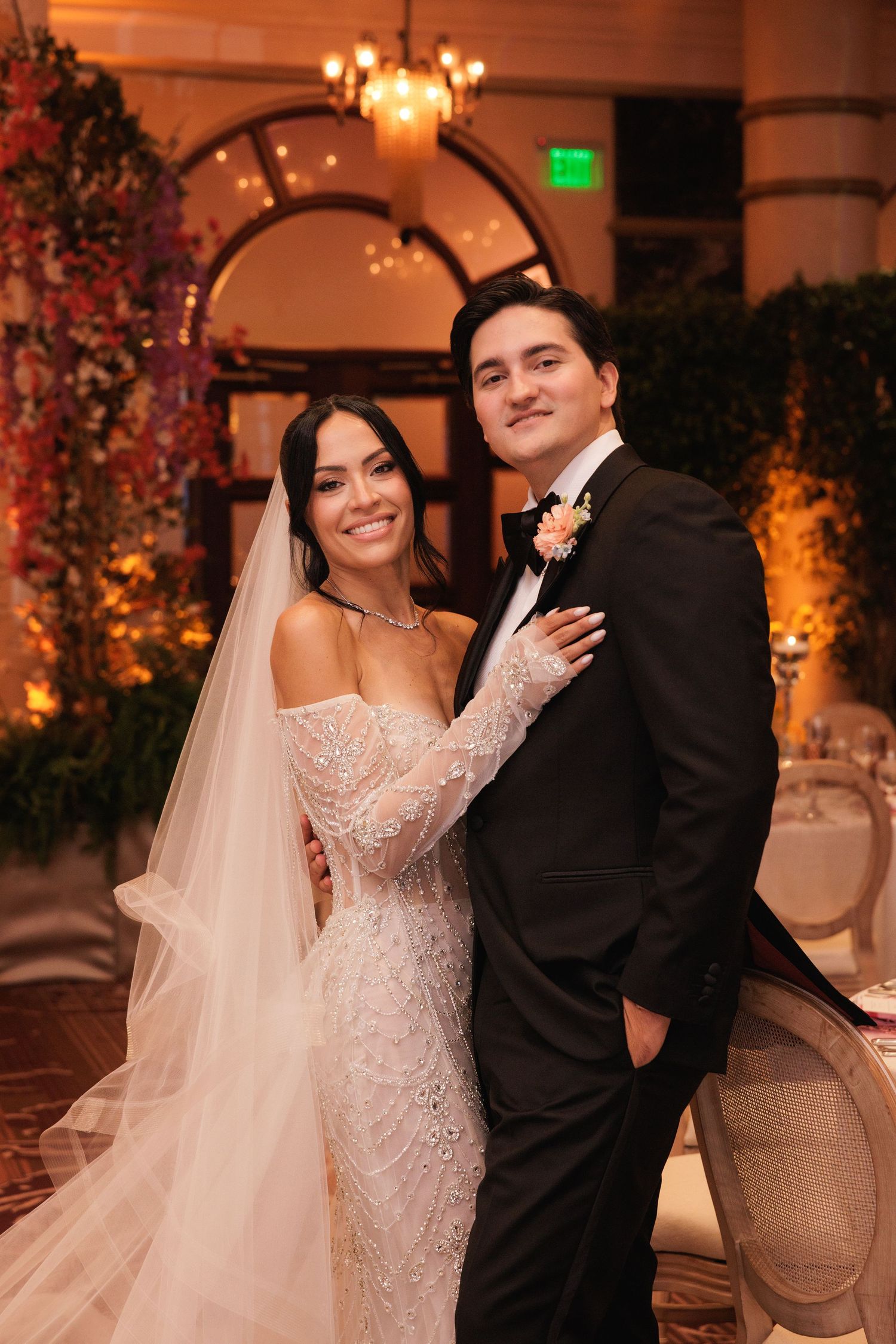 Romantic wedding couple poses in an elegant venue with warm lighting and floral arrangements.