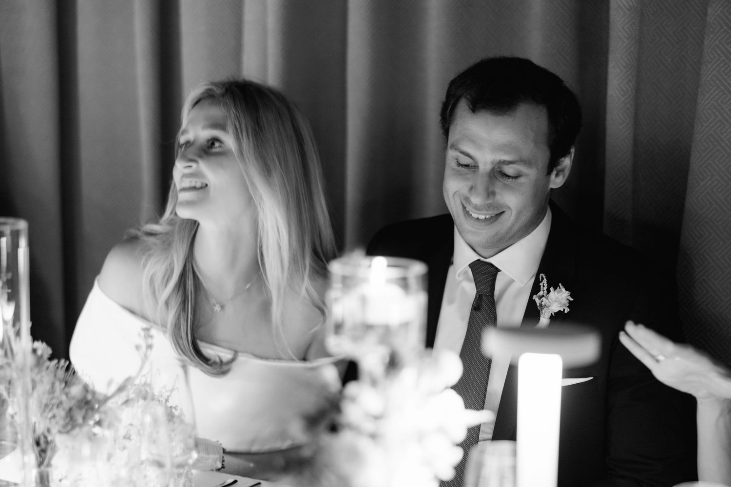 Wedding guests laugh and smile during an emotional toast at the reception in black and white.