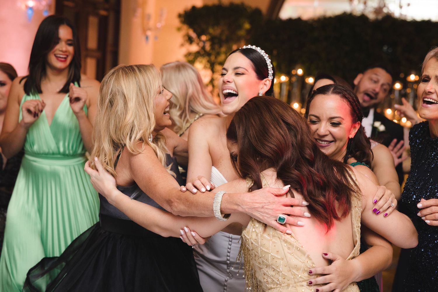 A group of wedding party guests sharing a joyful moment of laughter and hugs at a reception celebration.