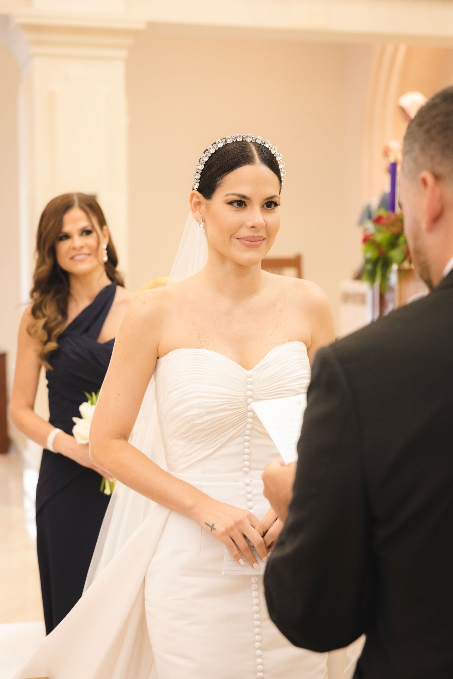 Couple dancing at a wedding reception in an elegant white ballroom with guests looking on in formal attire.