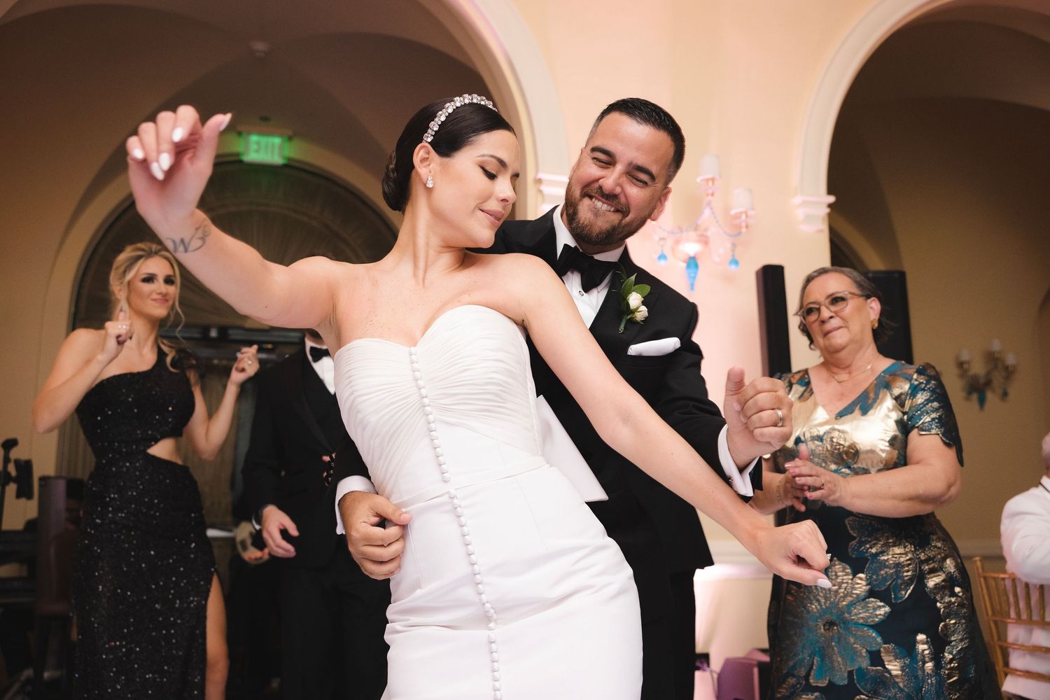 A bride and groom share a romantic dance at their wedding reception while guests watch and smile.