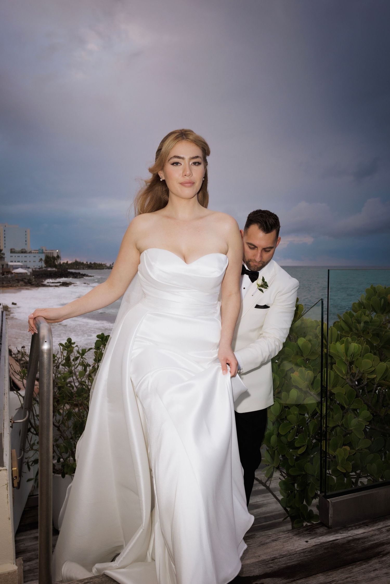 A couple shares an intimate moment during their wedding photoshoot on a seaside terrace.