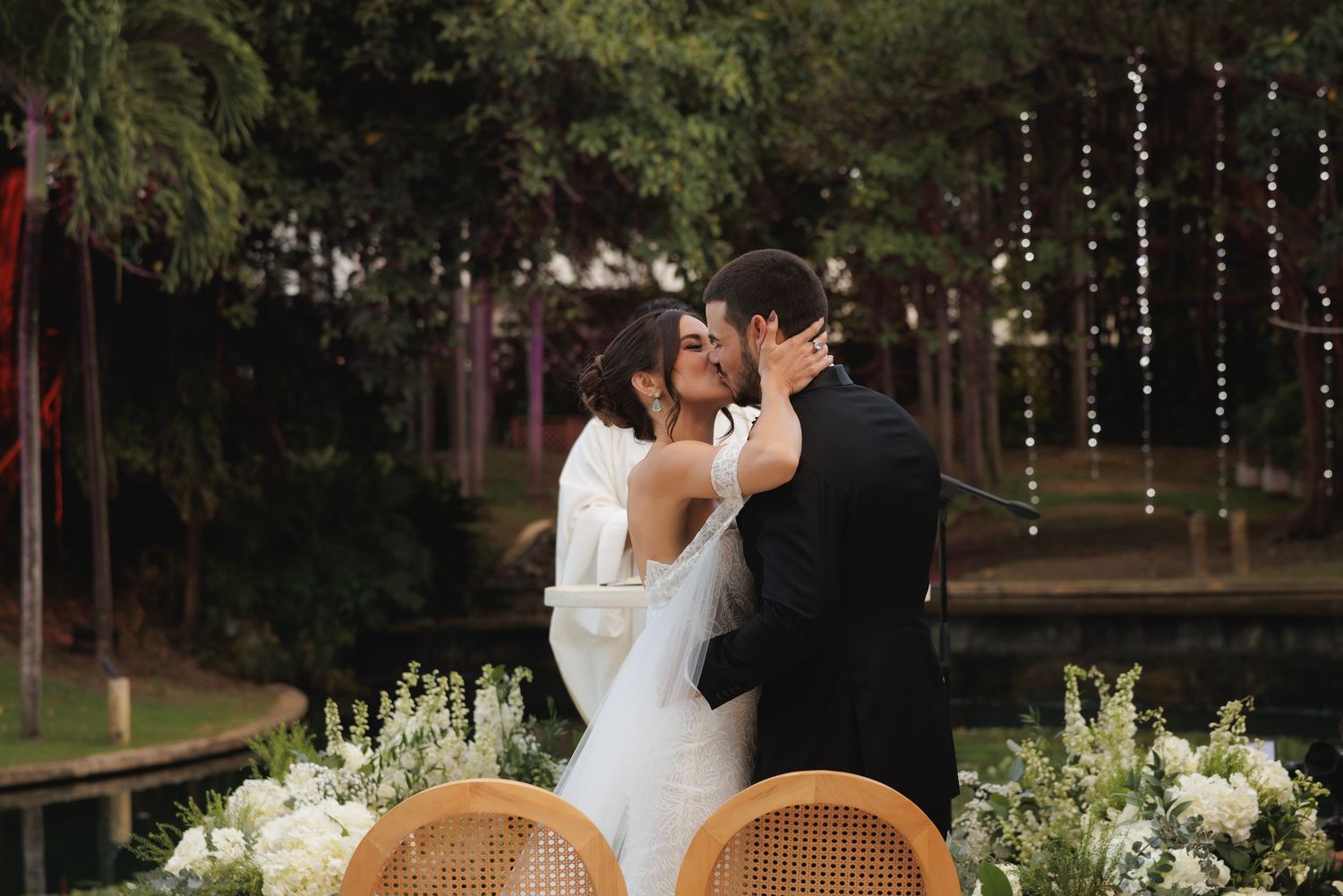 Romantic evening wedding reception with twinkling string lights and wooden chairs in garden setting.