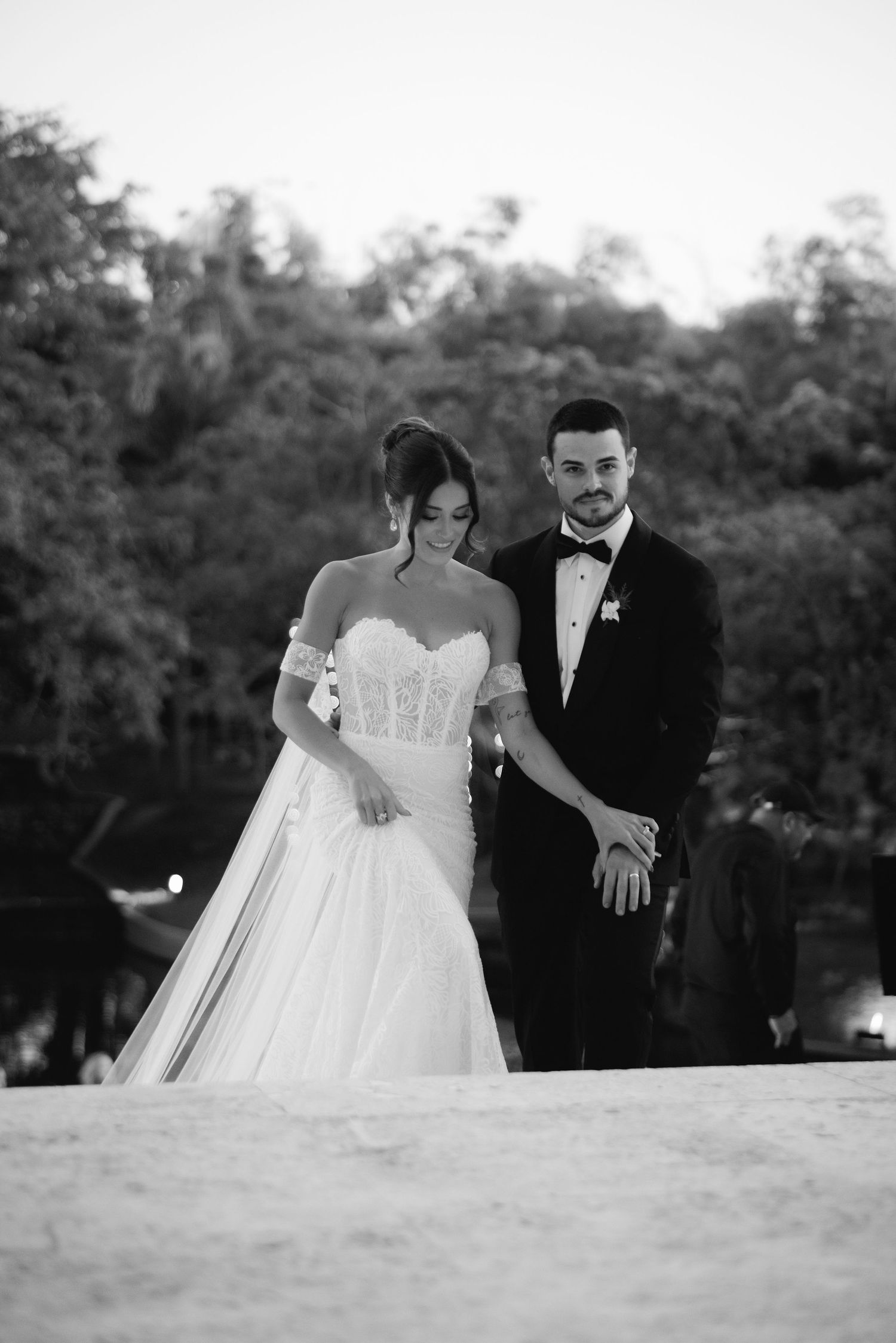 Black and white wedding portrait shows couple walking together on scenic outdoor path.