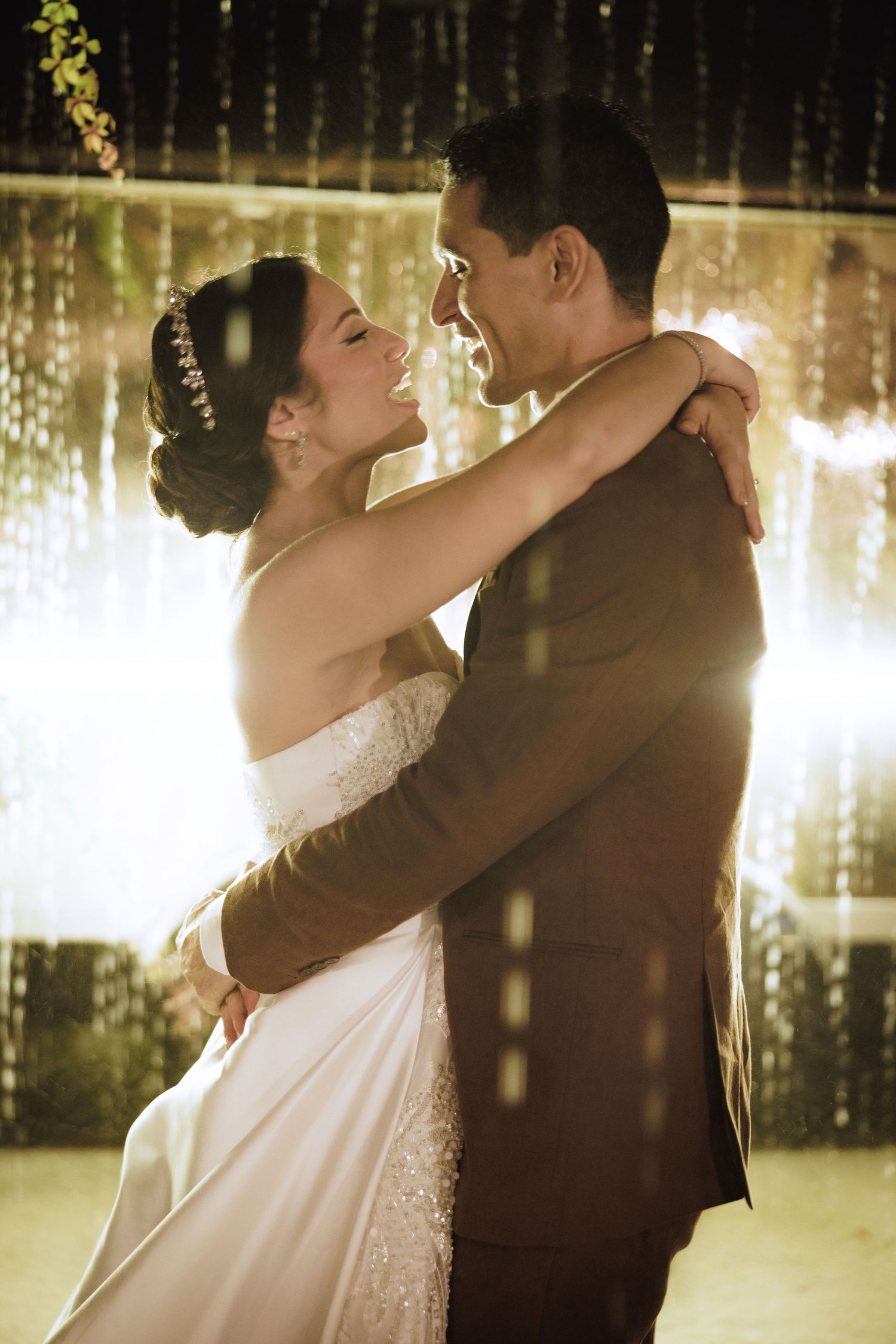 Newlyweds share an intimate dance moment beneath cascading fairy lights at their evening reception.