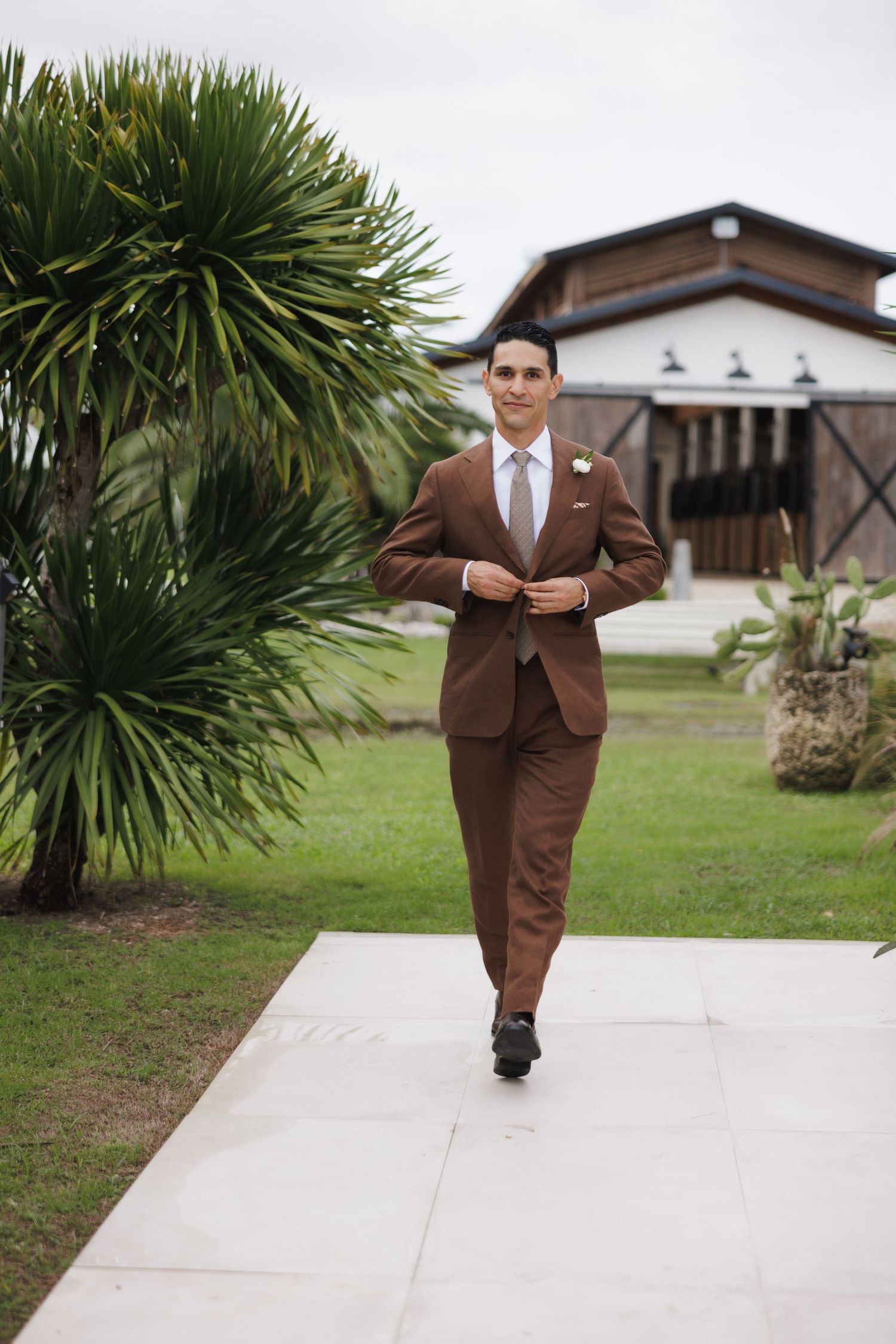 Person in brown suit walks confidently on pathway near tropical plants.