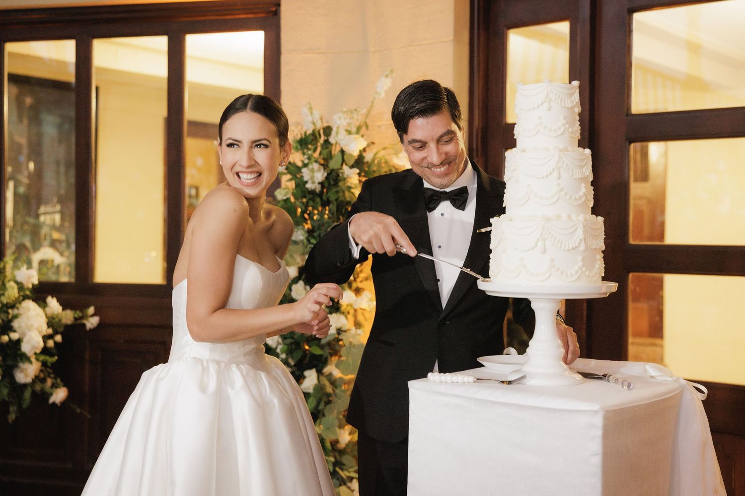 Wedding couple cuts their elegant white tiered cake together at reception.