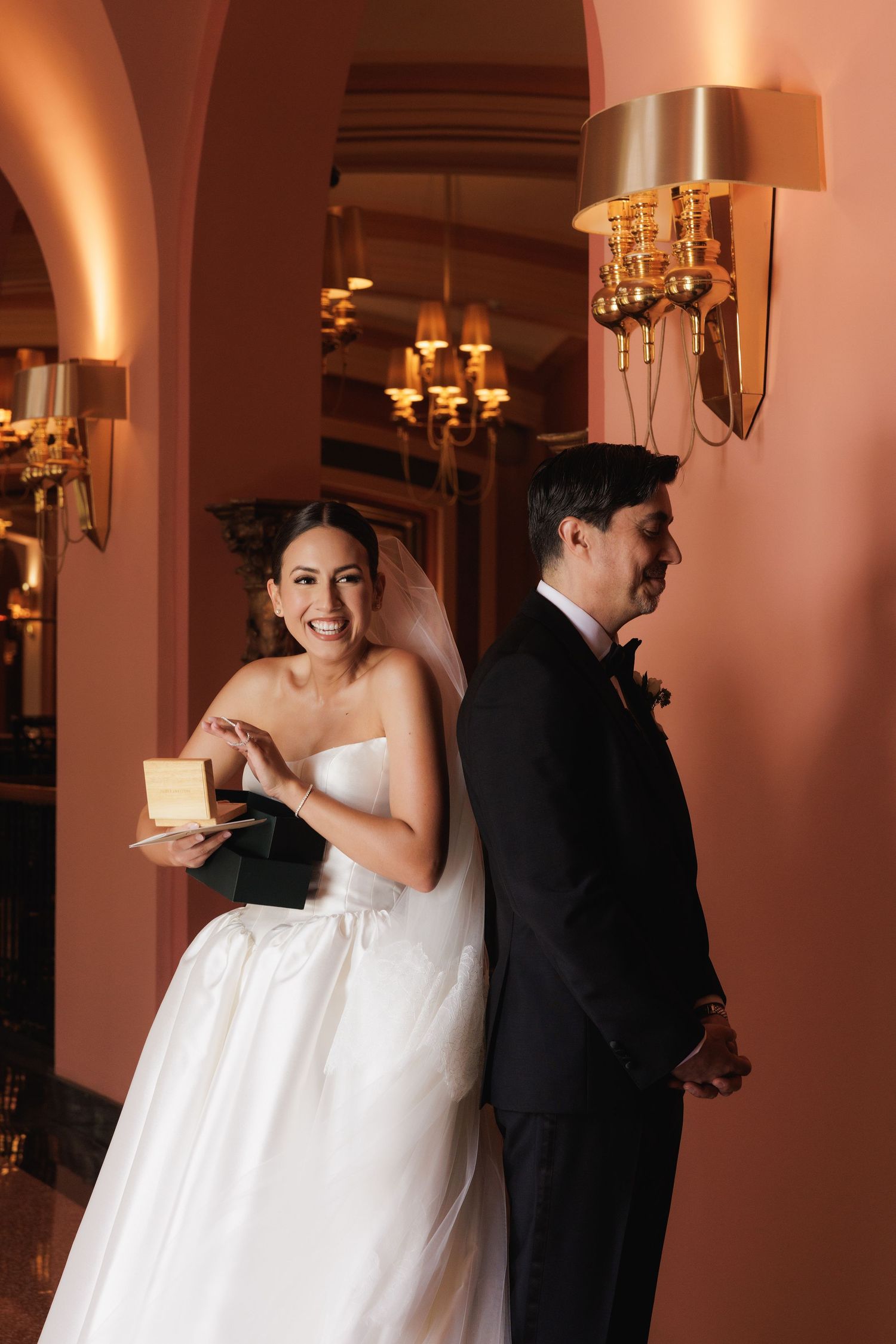 A bride and groom share a romantic moment in an elegant ballroom with warm lighting and wall sconces.