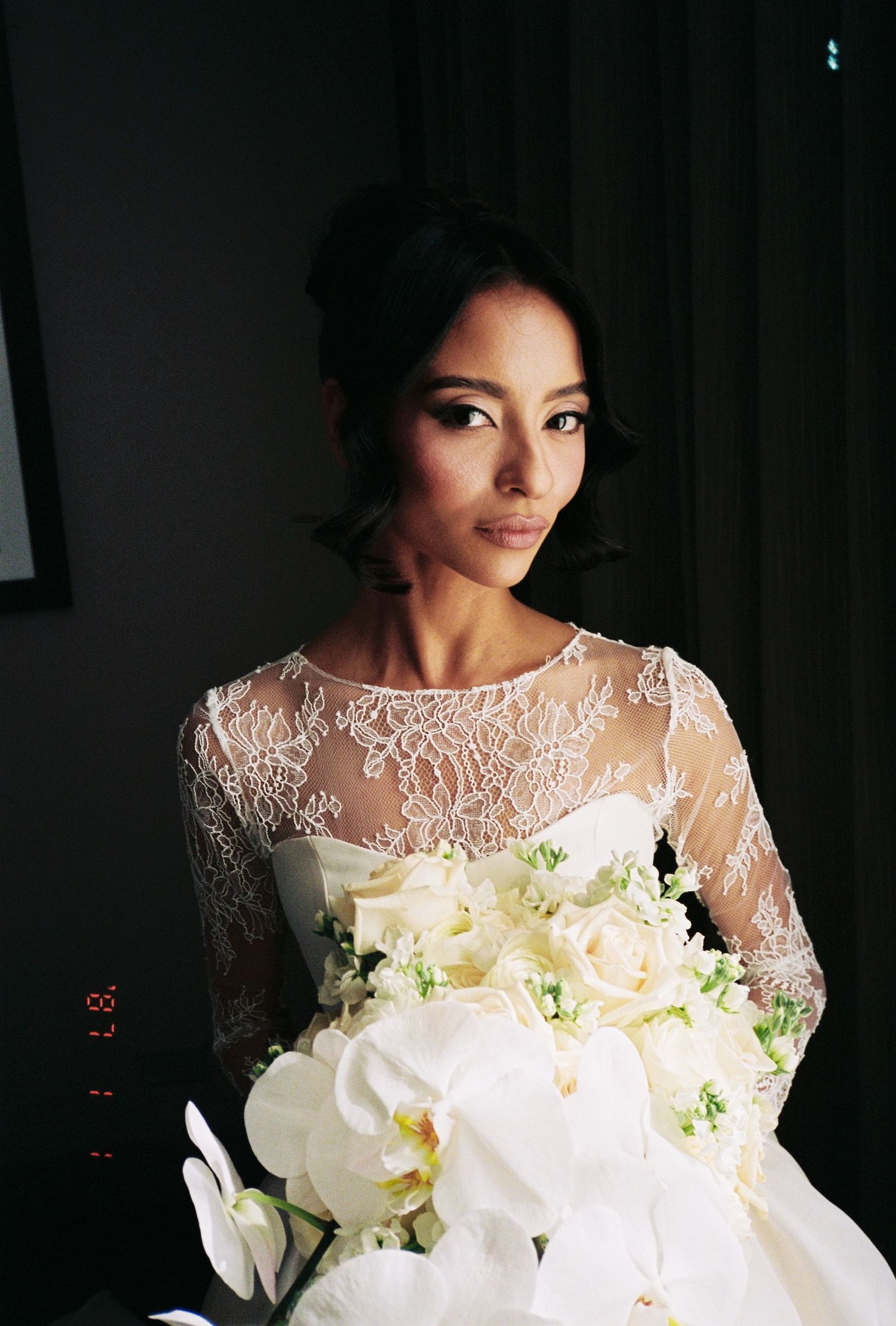 Elegant bride in lace wedding gown holding white orchid bouquet.