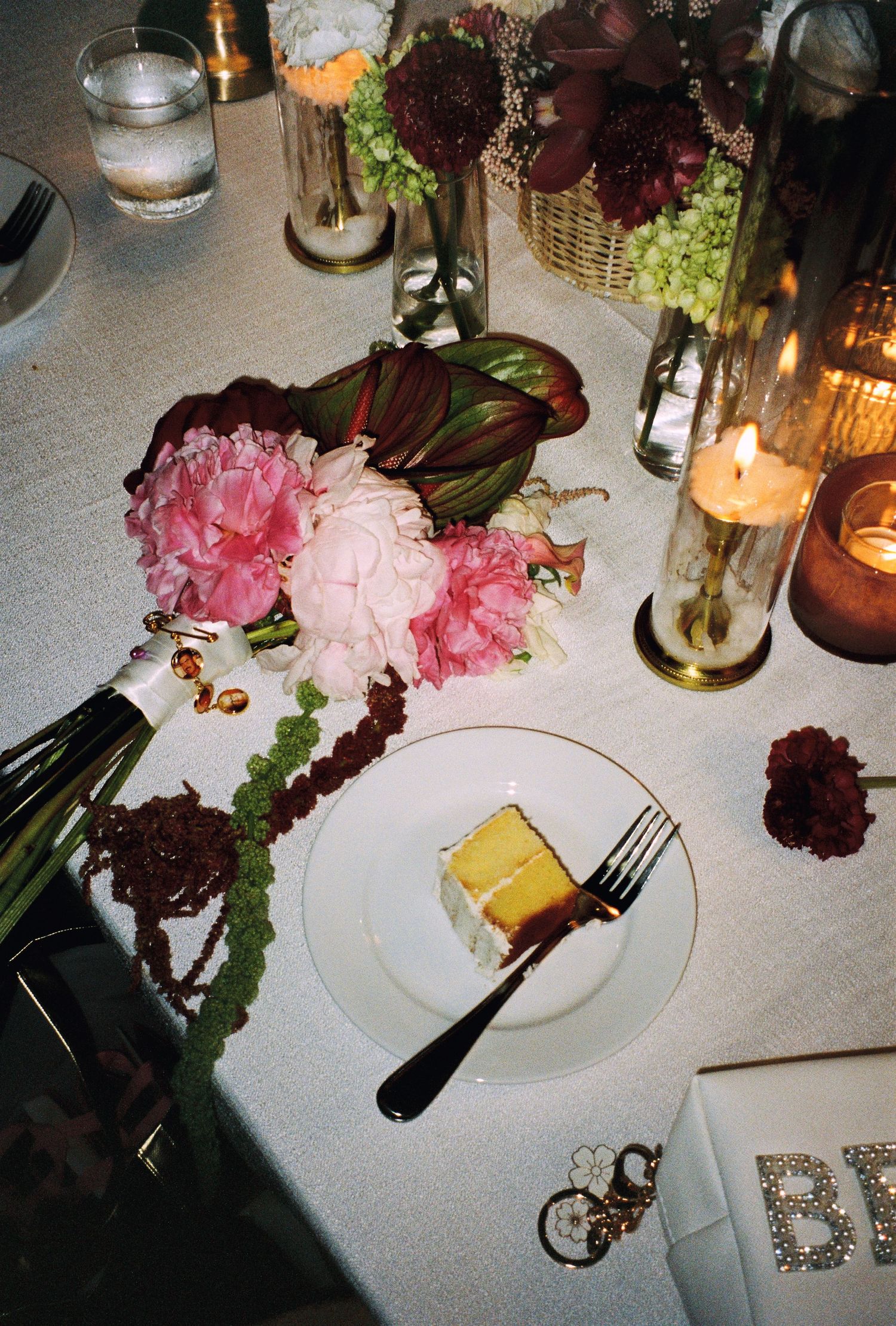 Wedding reception table with pink peonies, yellow cake slice, candles, and floral arrangements.