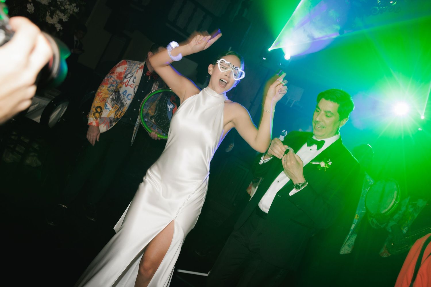 Wedding party dancing under vibrant green and blue lighting effects at a reception.