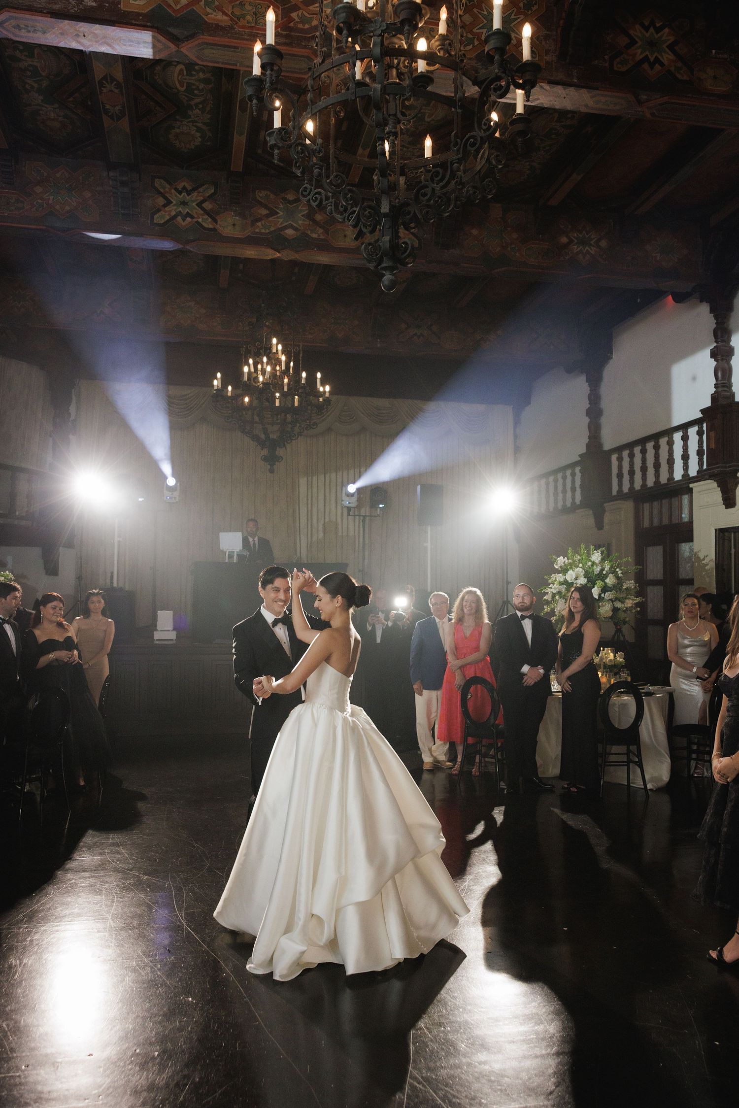 Wedding reception in a grand ballroom with chandeliers and atmospheric lighting.