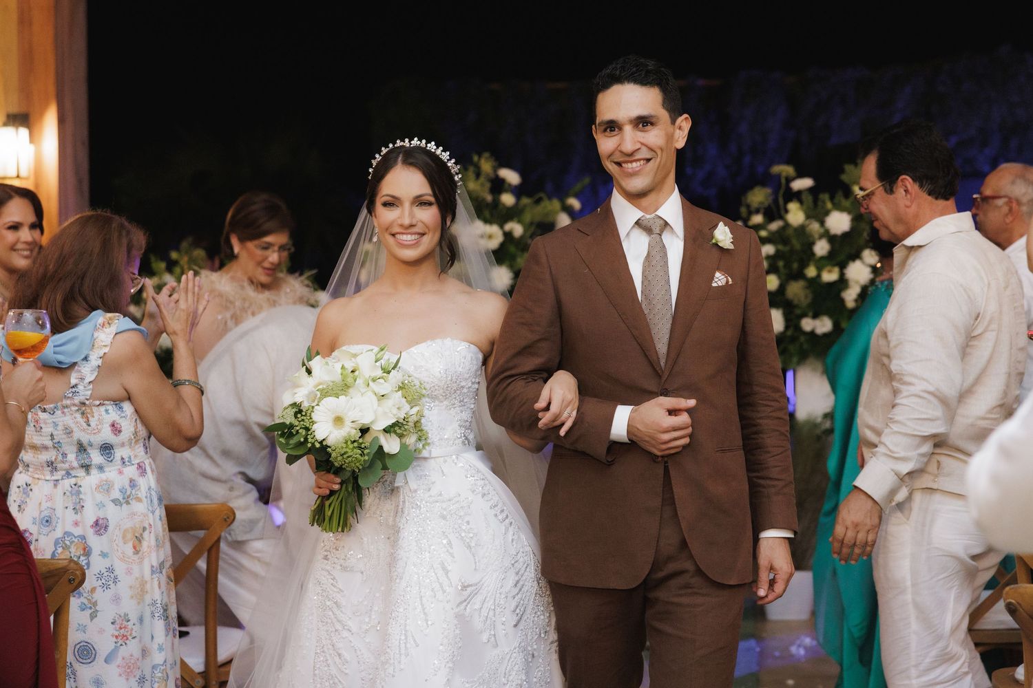 Wedding celebration with guests in formal attire gathered around floral decorations.