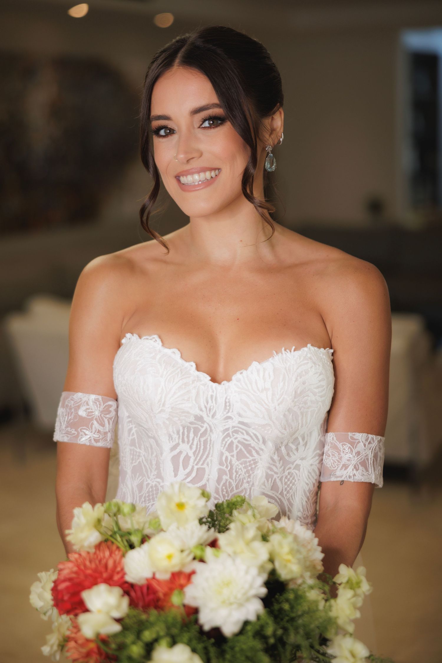 A radiant bride in a strapless lace gown holds a colorful bouquet featuring red and white flowers.