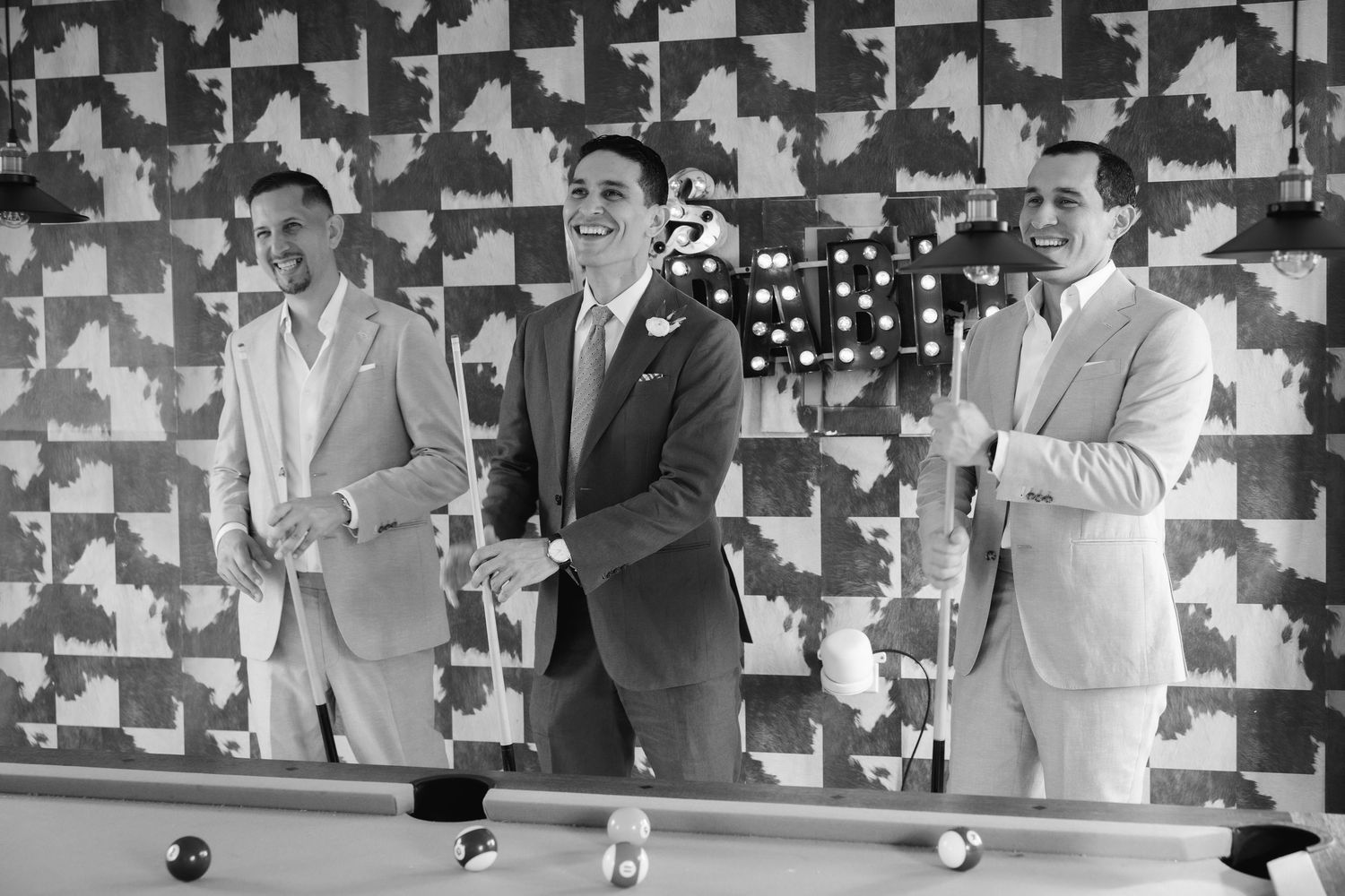 Wedding party in formal attire stands against geometric black and white backdrop.