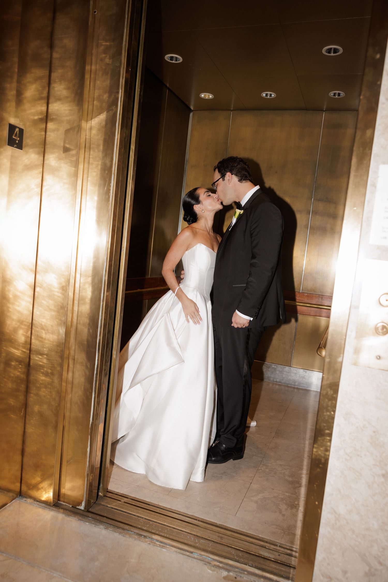 A romantic wedding couple shares a kiss in an elegant gold-toned elevator.