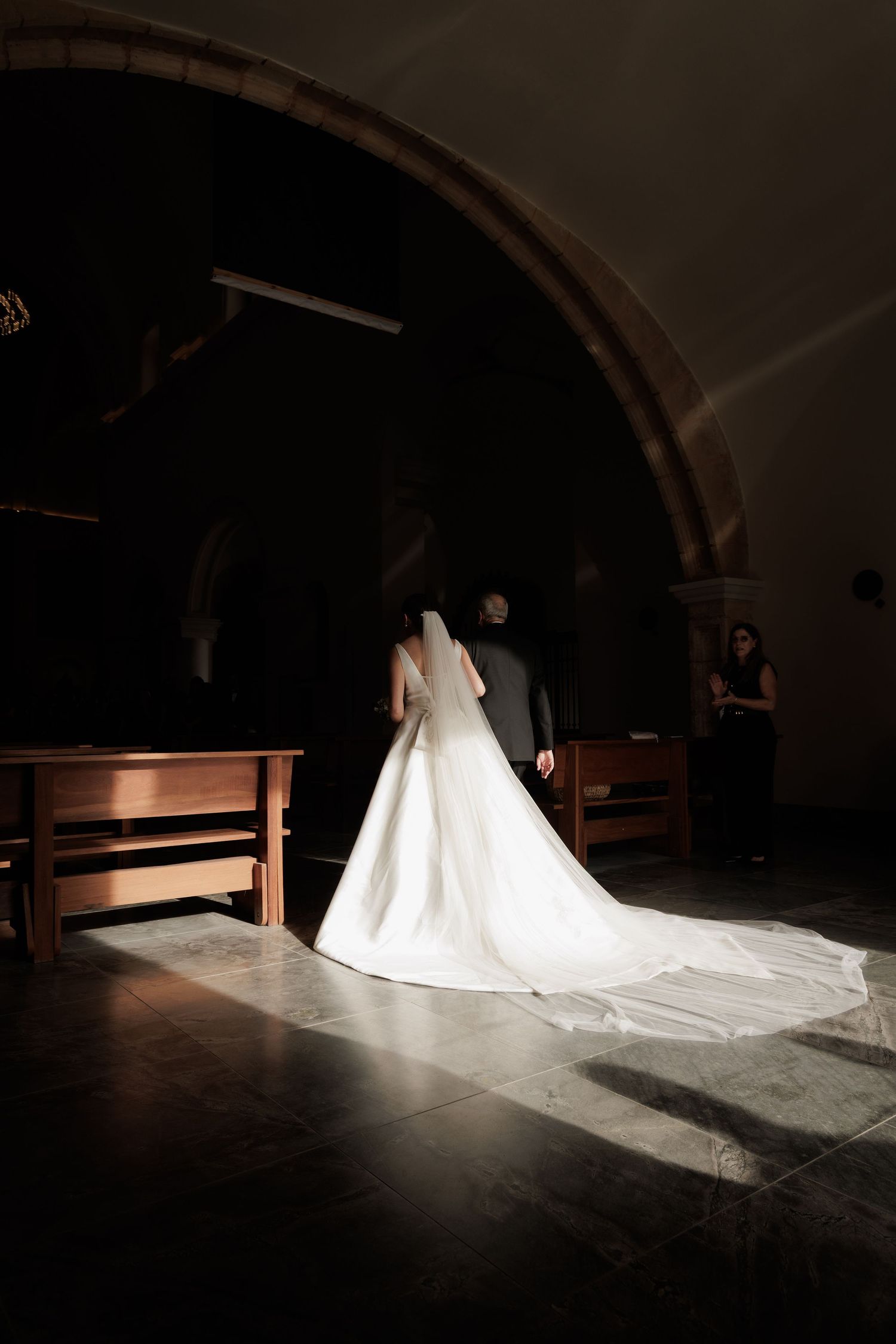 Wedding dress with long train photographed in silhouette inside a dimly lit church.