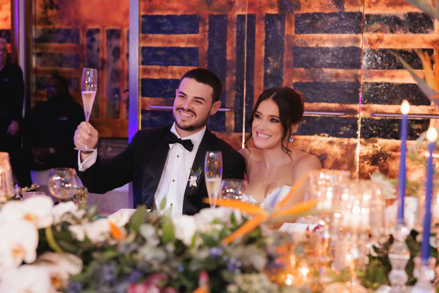A festive dining scene with elegant table settings, glowing candles, and decorative floral arrangements at a formal event.
