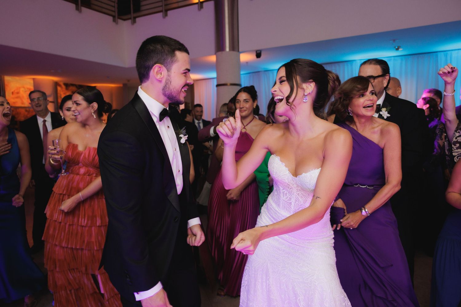 Wedding guests dance and celebrate together on a colorful dance floor at an indoor reception venue.
