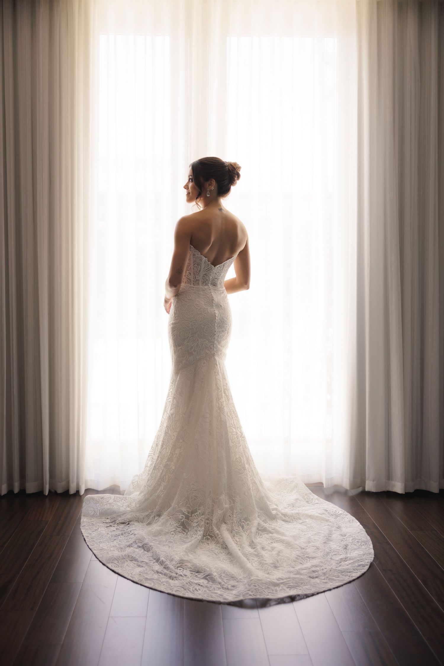 A wedding dress silhouetted against bright window light on dark hardwood floors.