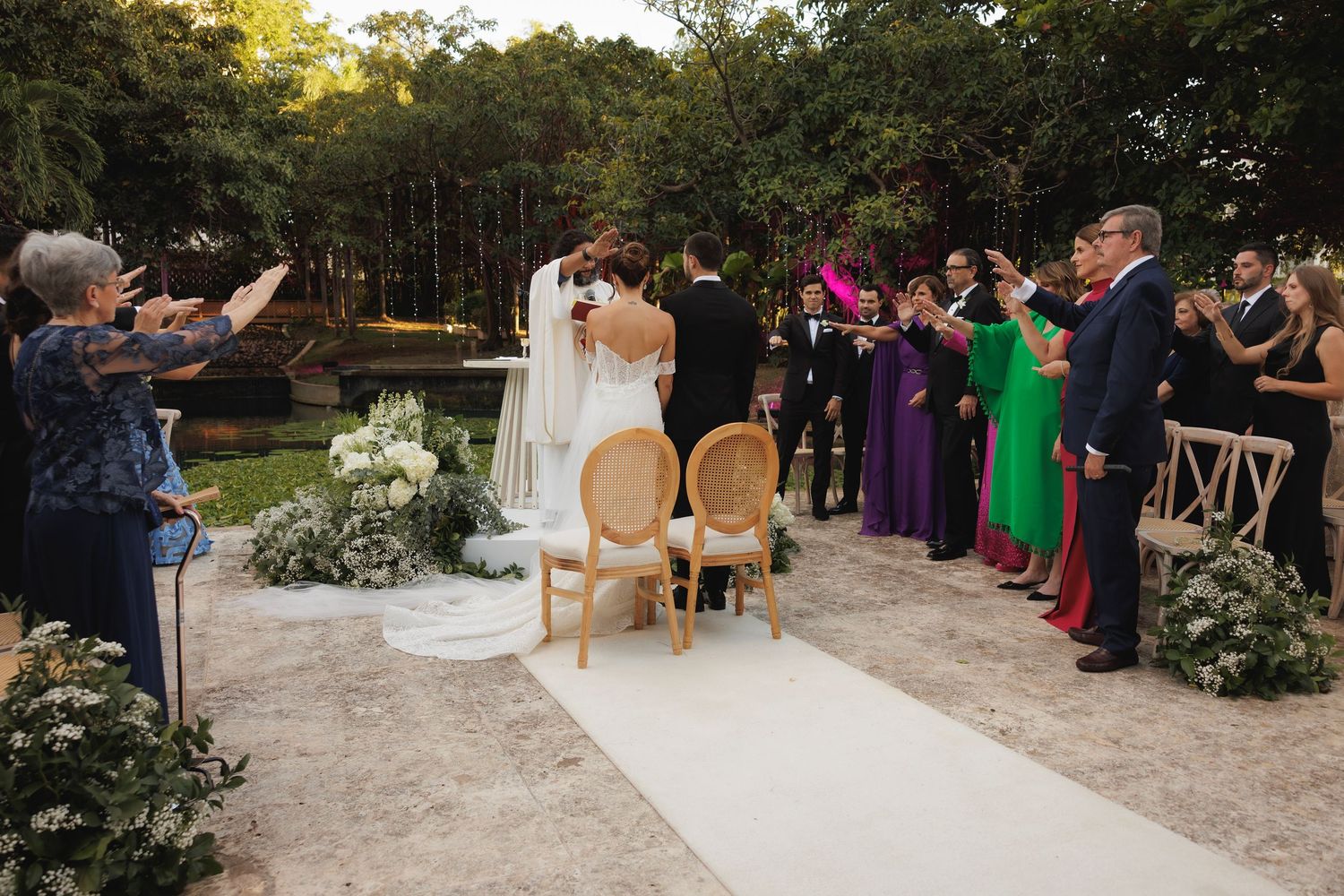 Wedding ceremony setup outdoors with white chairs, floral arrangements, and guests celebrating the occasion.