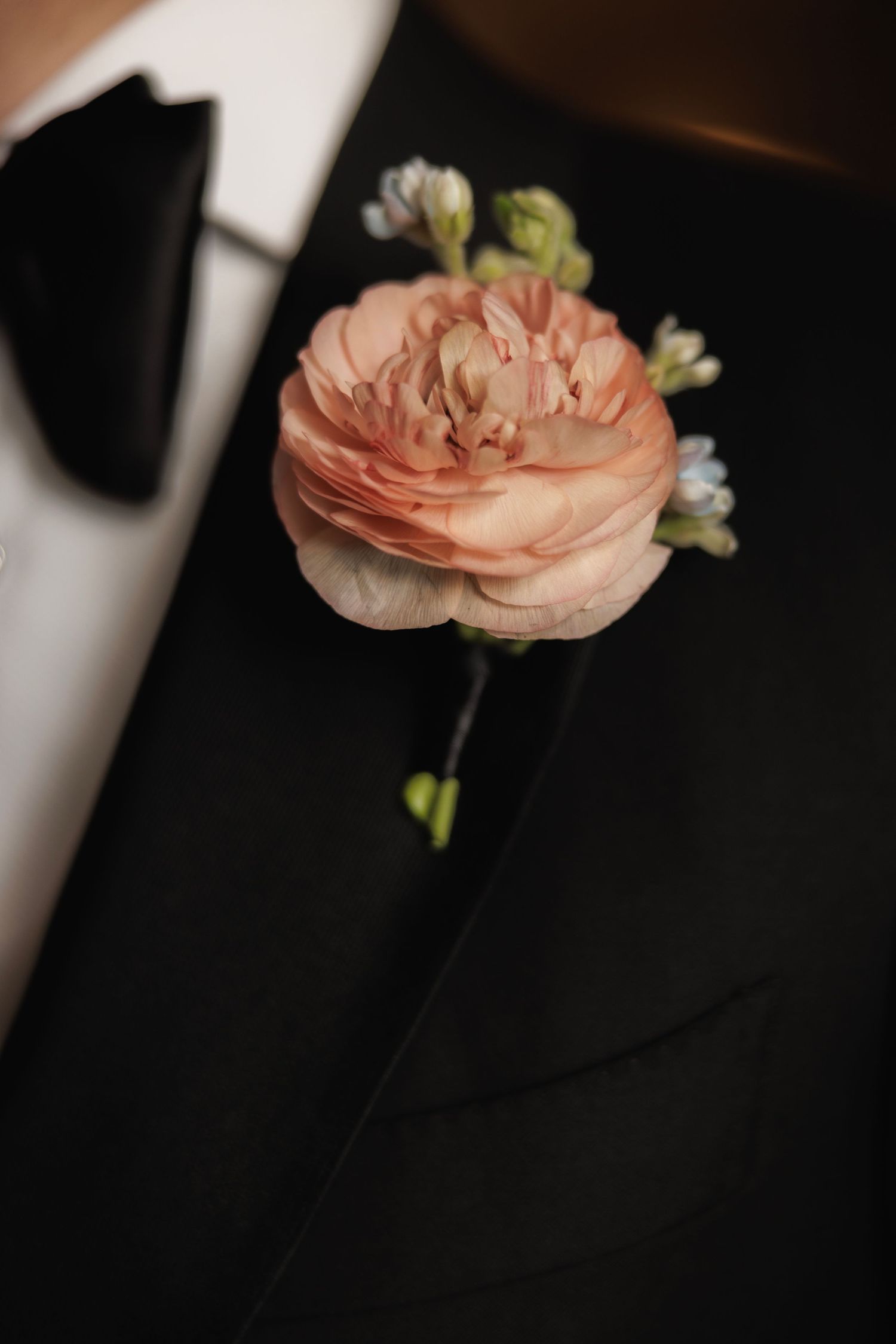 A delicate peach-colored boutonniere with small buds stands out against a dark background.