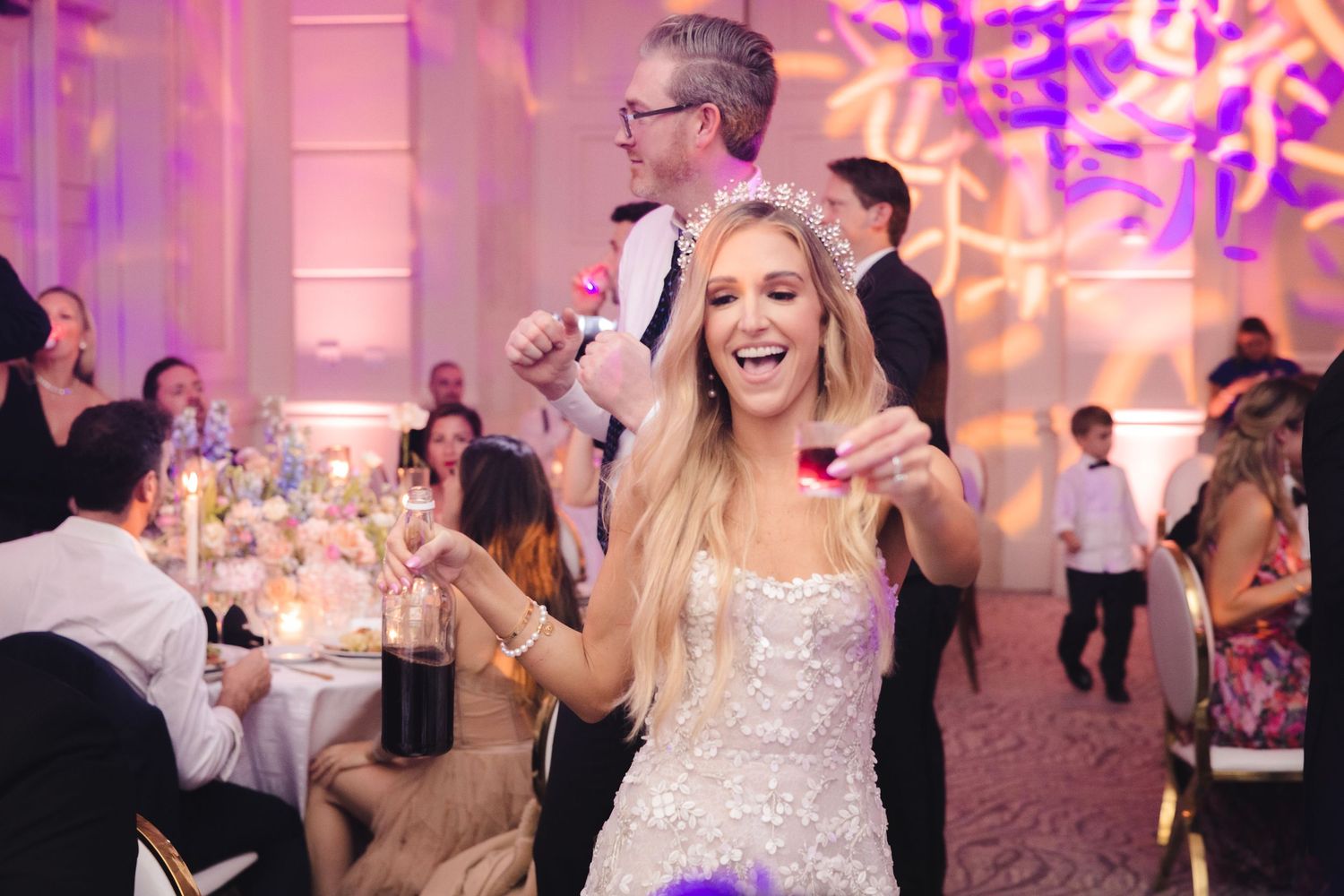 Reception guests enjoy dancing and entertainment in a beautiful pink-lit ballroom setting.