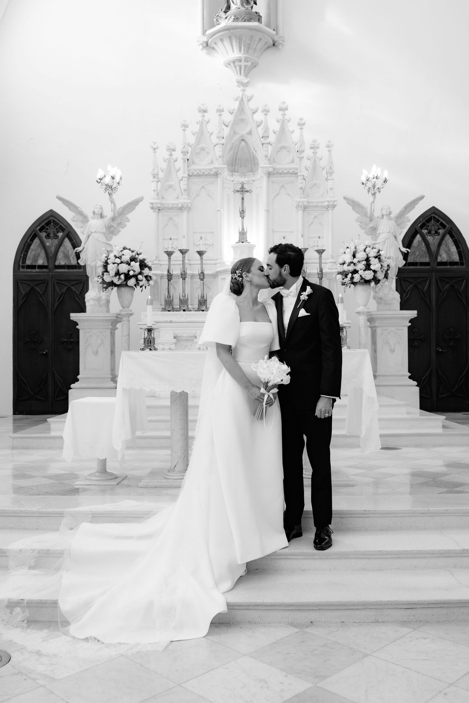 A black and white wedding portrait capturing a romantic moment in front of an ornate church altar.