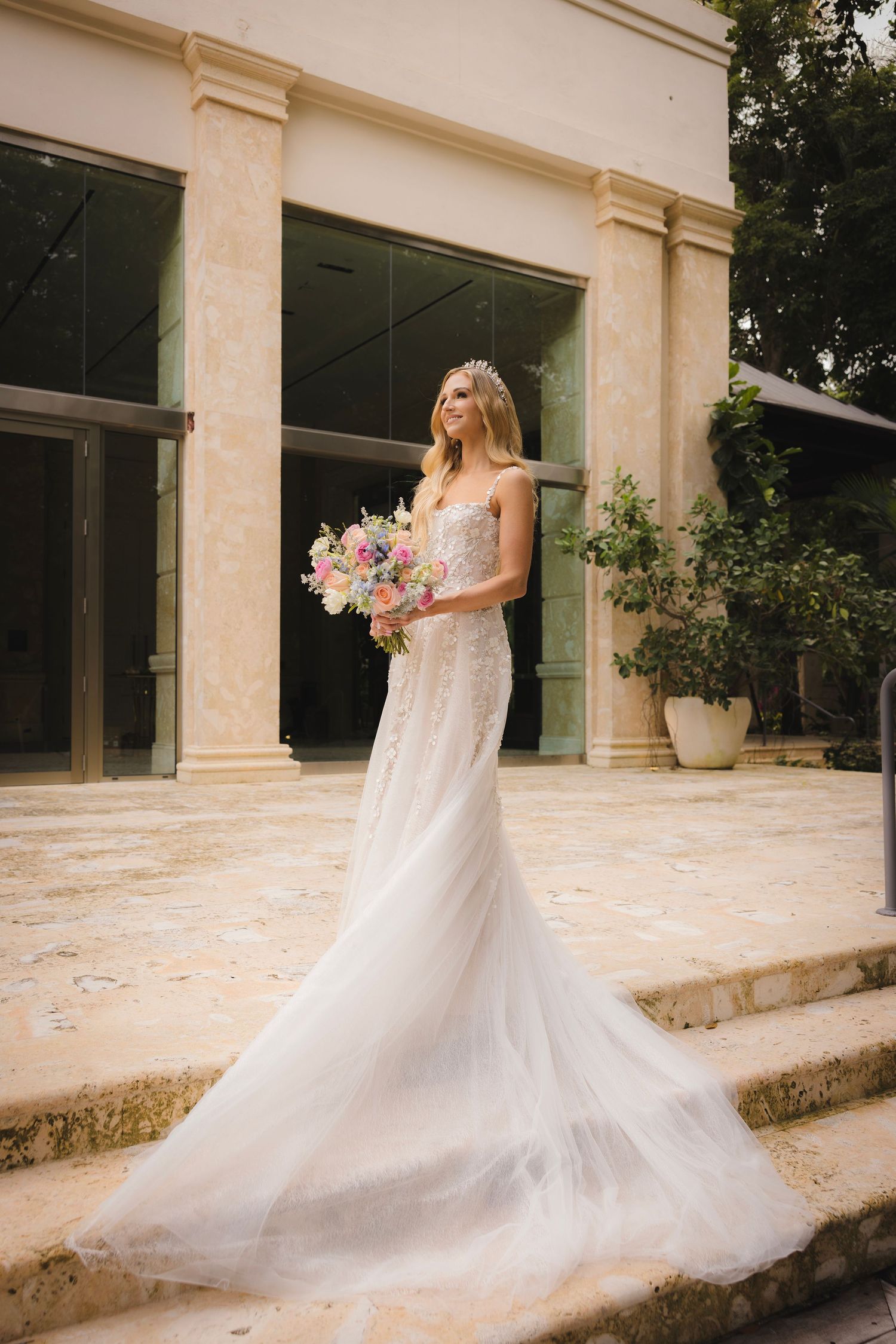 Elegant white wedding gown with flowing train and delicate lace details captured at classic architectural venue.