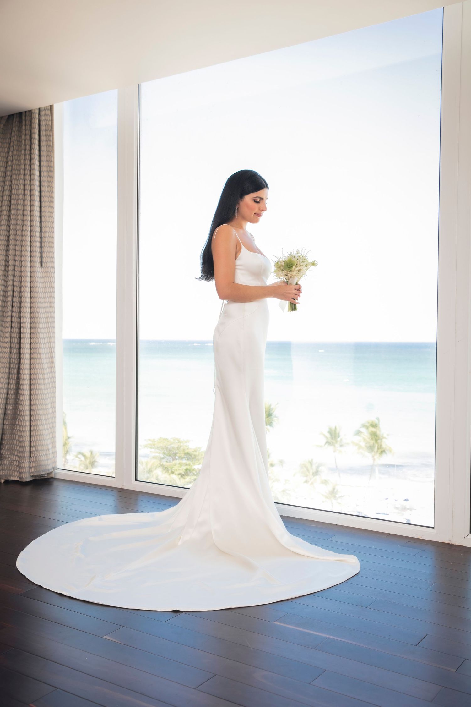 White wedding dress with long flowing train against wooden floor and ocean backdrop.