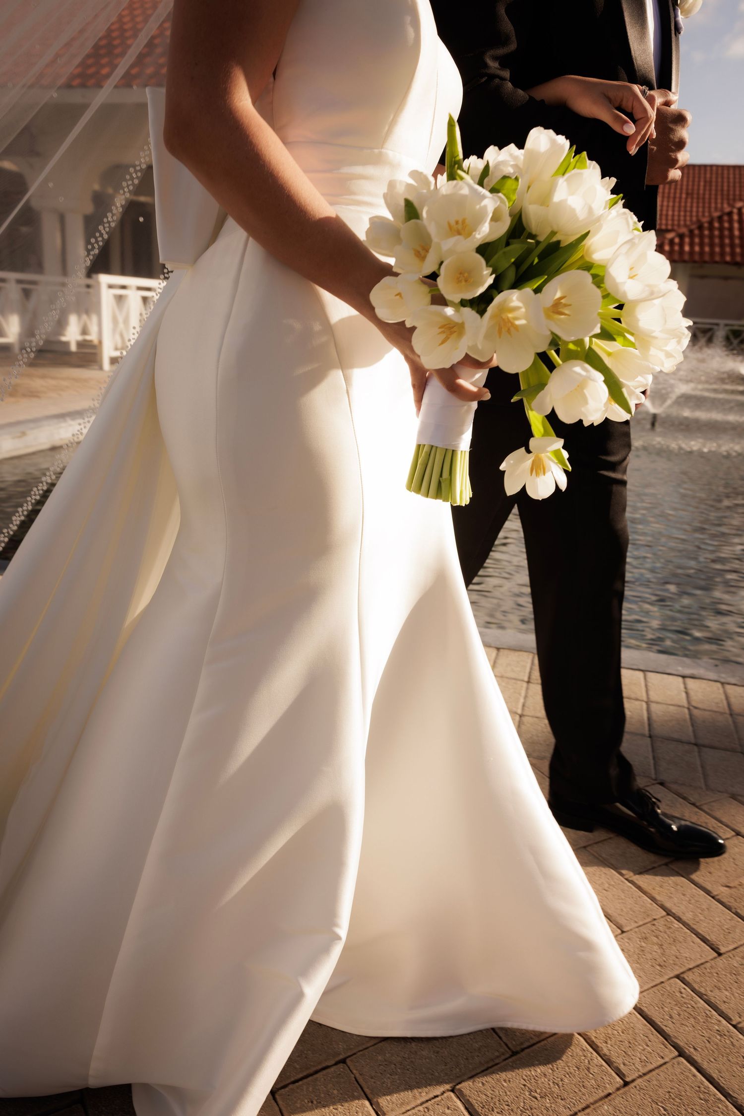 A series of cropped wedding photos showing white bridal gown details and bouquet of white lilies against stone pavement.